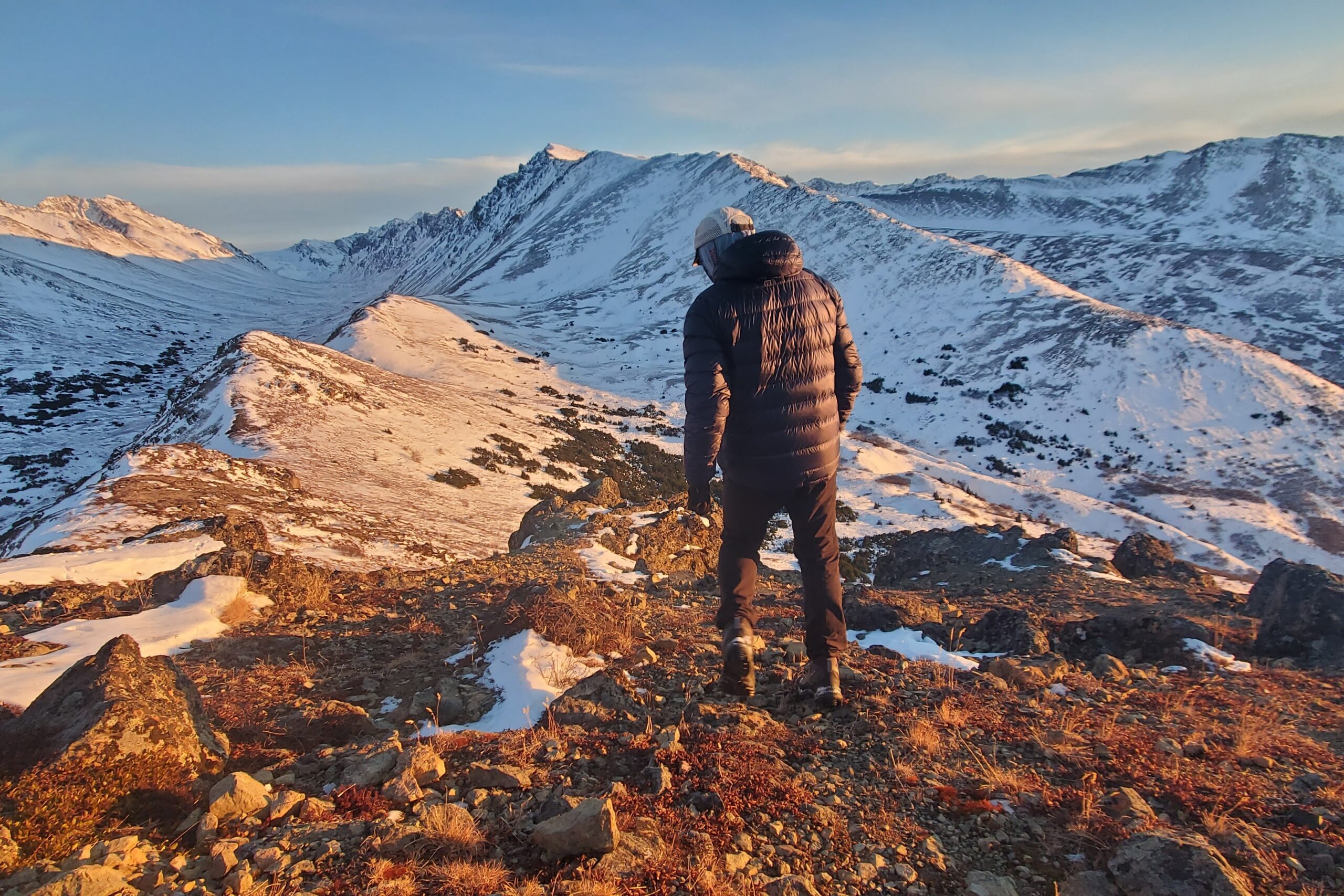 A man walks down a mountainside at sunset