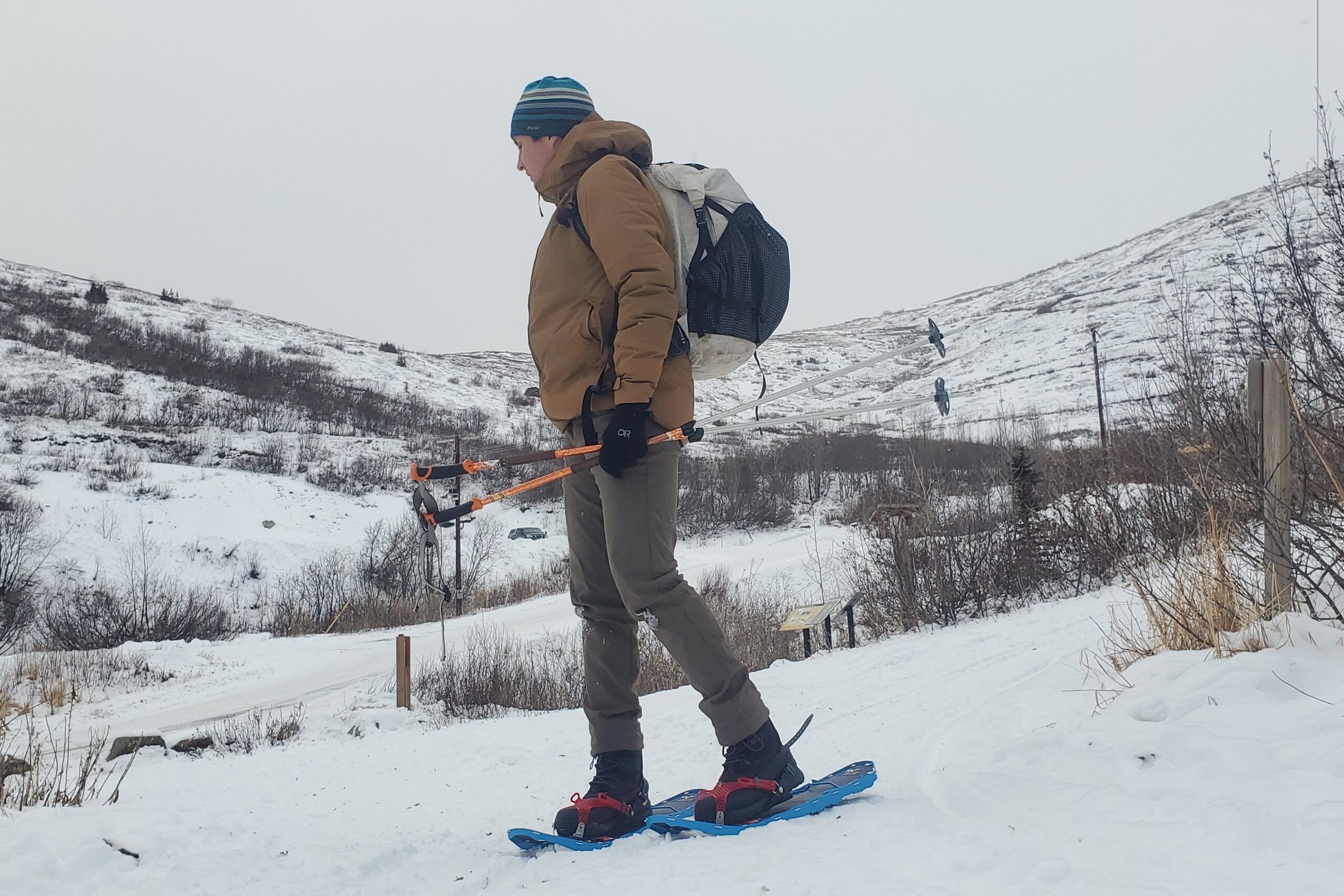 A man snowshoes, holding poles.