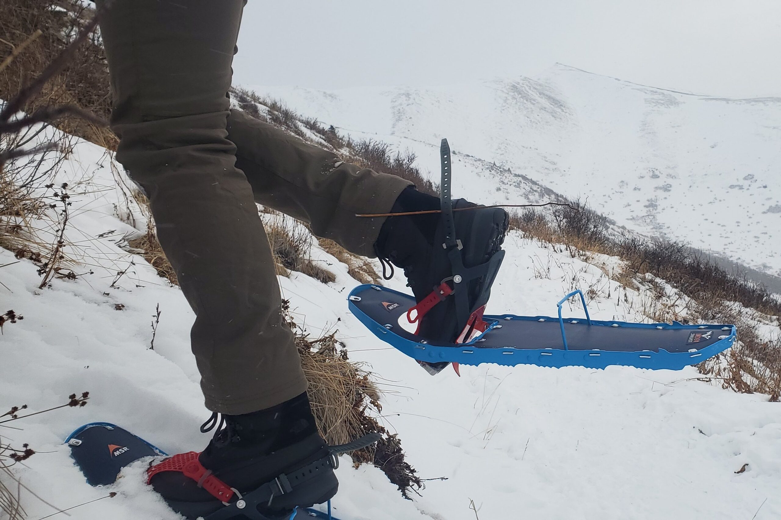 A man walks up a steep hill wearing snowshoes.