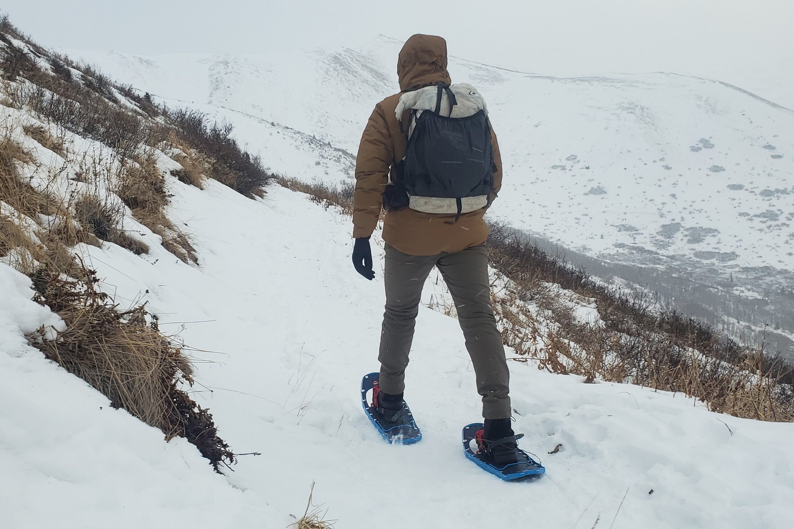 A man walks along a trail with mountains in the background.