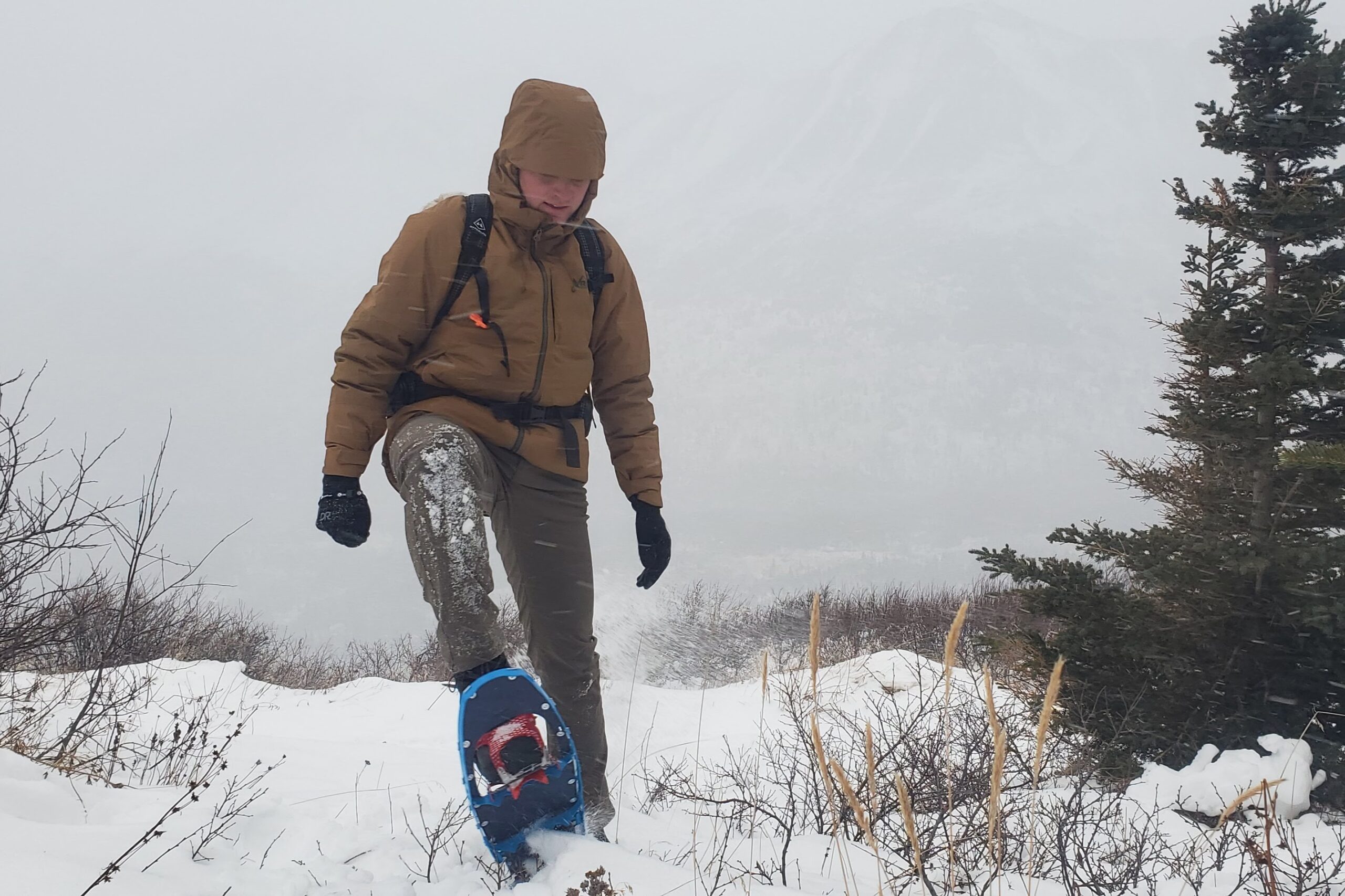 A man walks uphill in snowshoes in a blizzard.