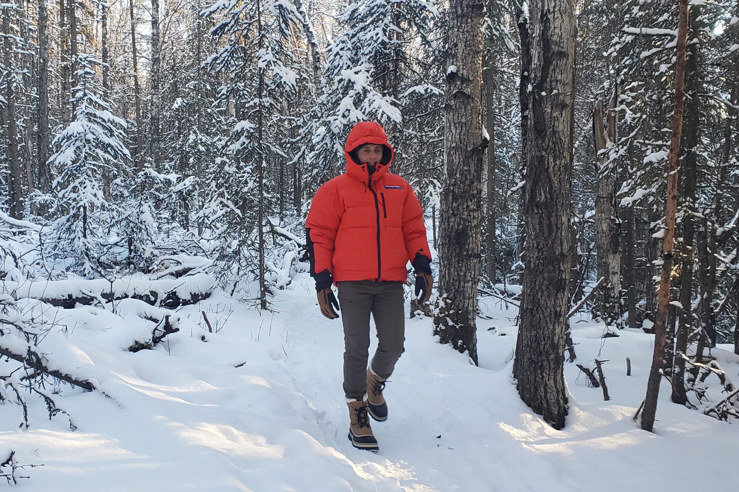 A man walks in a red down jacket through a snowy forest