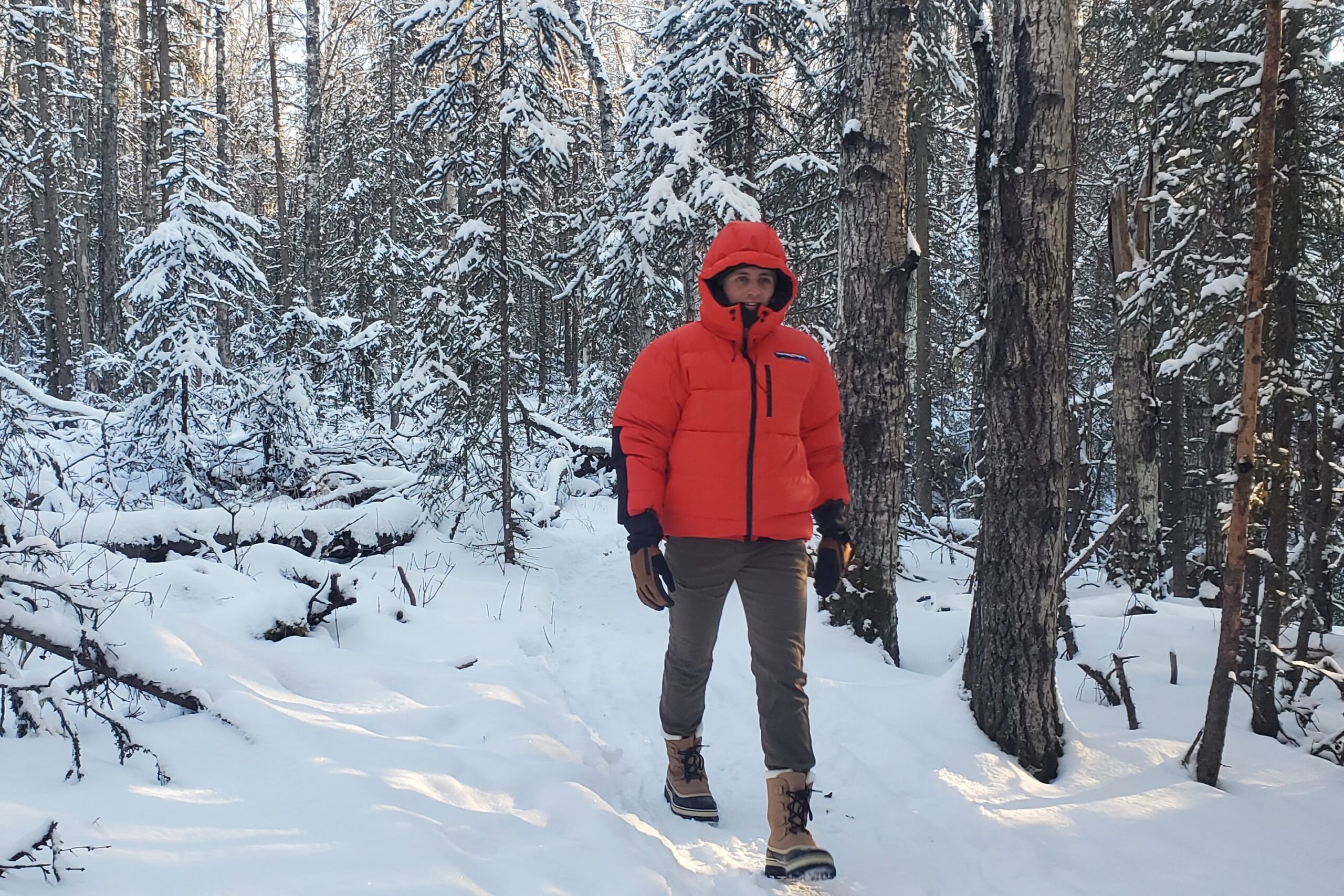 A man walks down a forested trail in the snow.