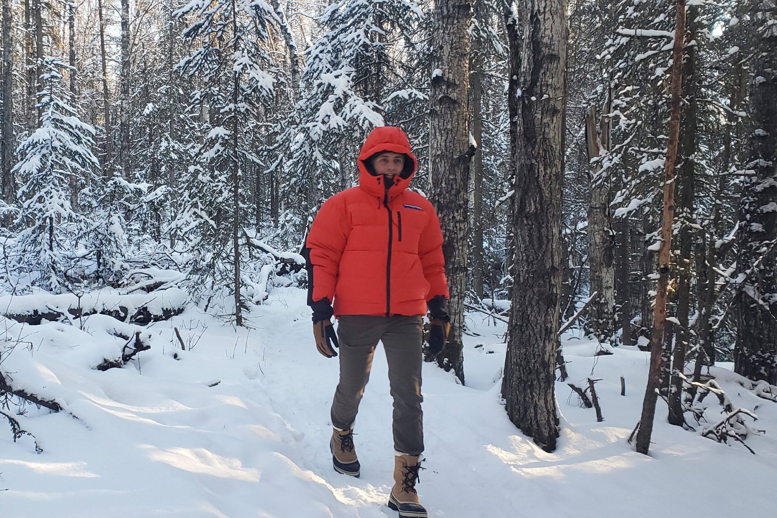 A man in a red coat walks through a snowy forest