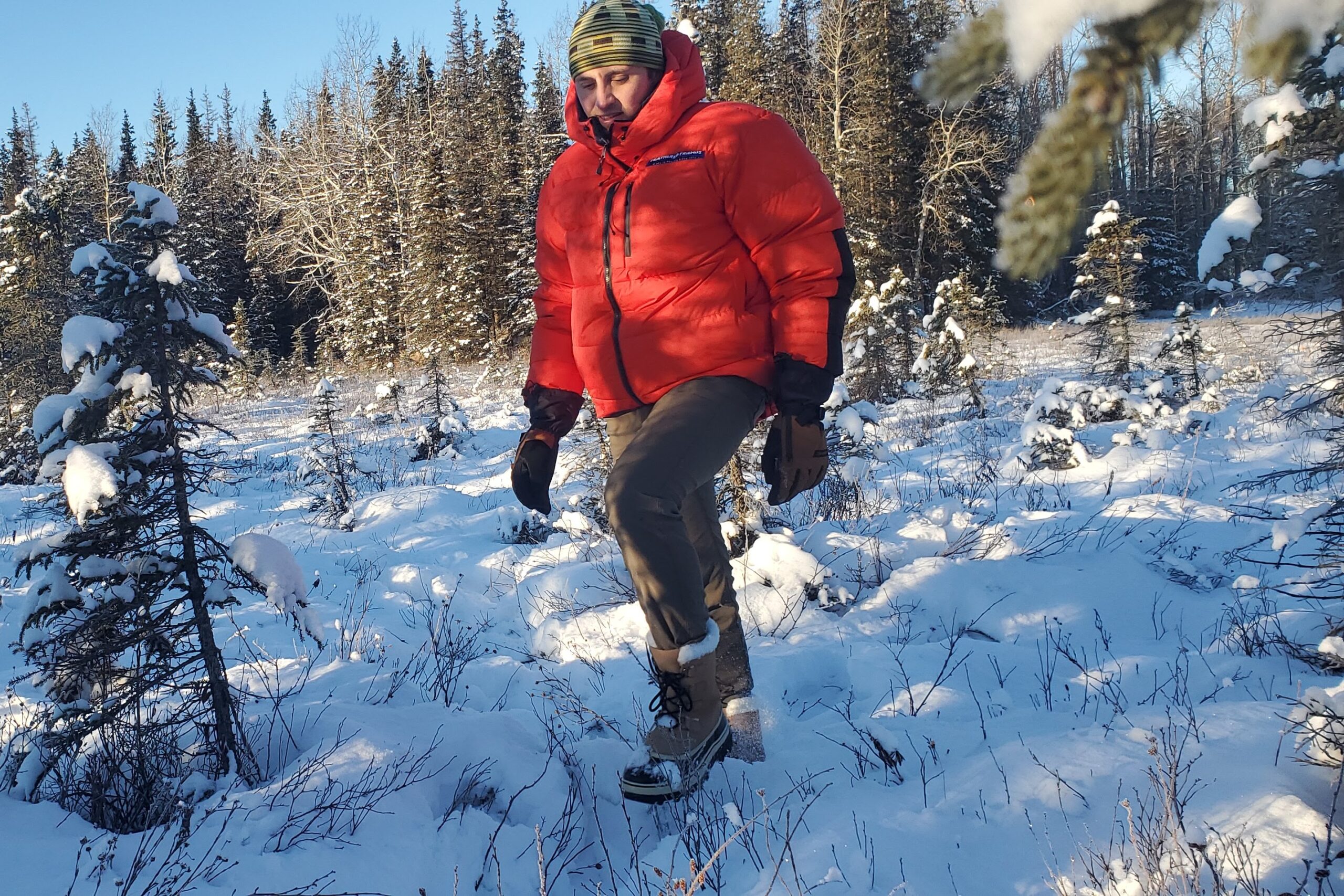 A man walks though a snowy meadow wearing winter gloves.