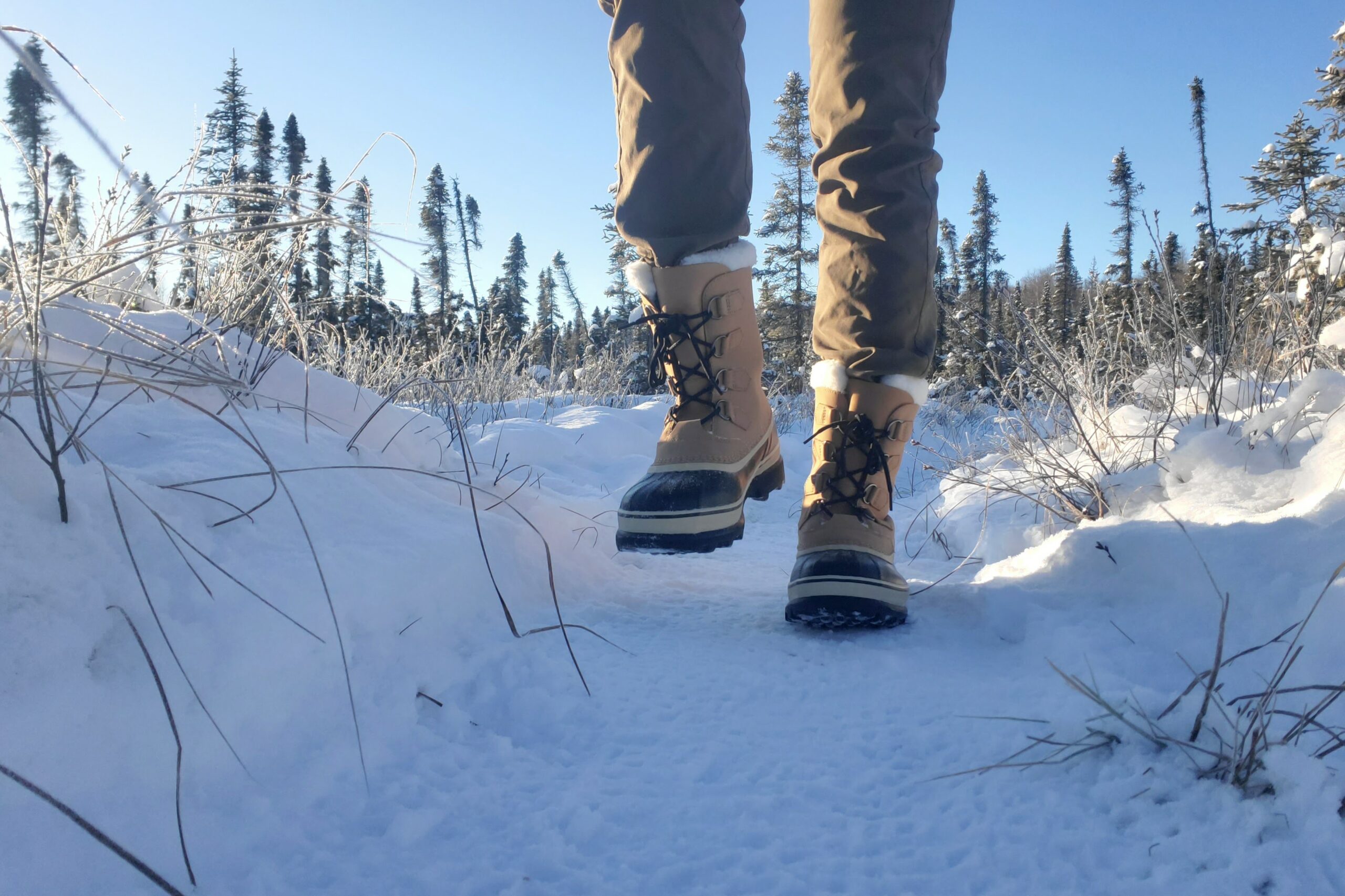 A closeup of winter boots walking toward the camera at ground level.