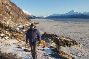 A man walks on a rocky ridge above a frozen ocean.