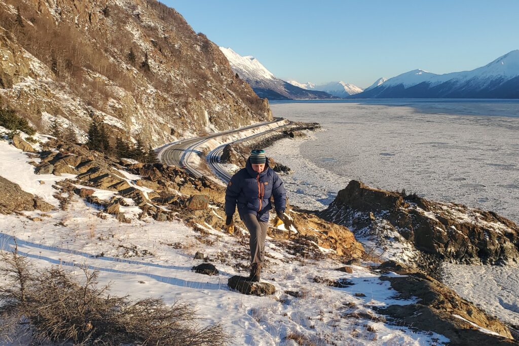 A man walks along a mountainside over a frozen ocean view.