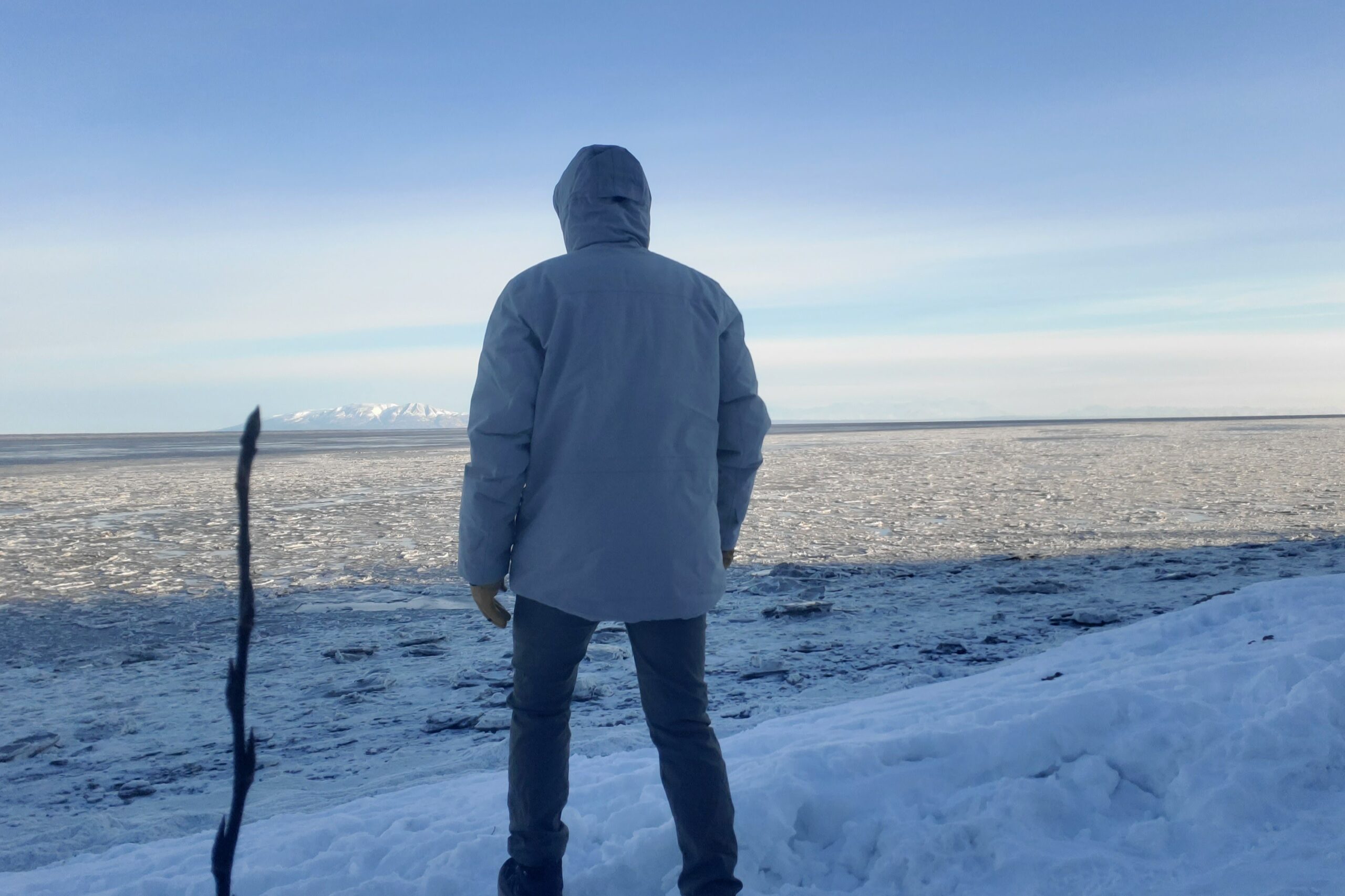 A man walks away from the camera on an icy shoreline.