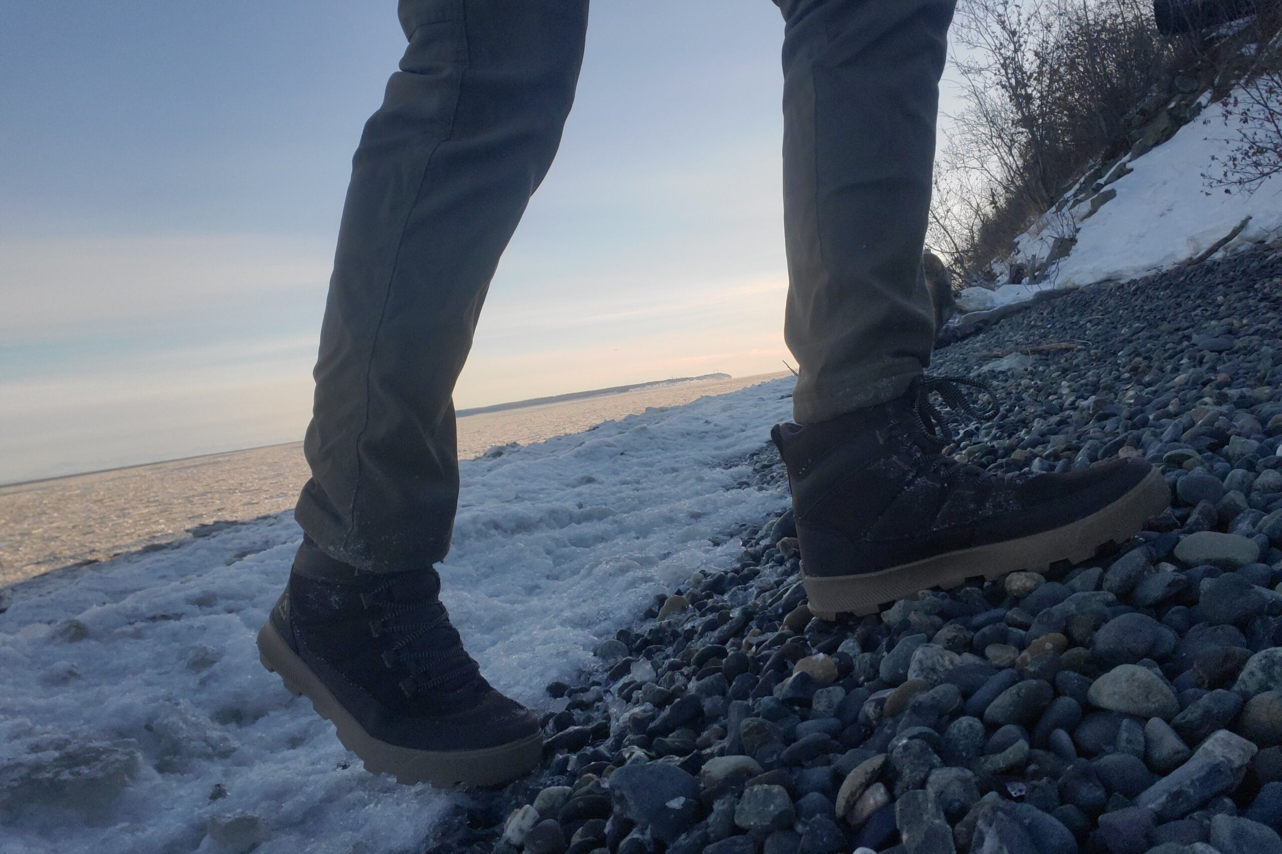 A closeup of boots walking up ice covered rocks.