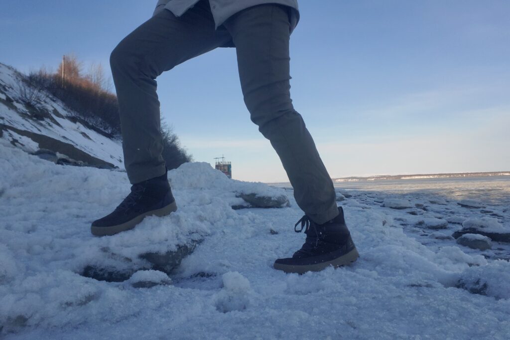 A man walks up large chunks of ice along the ocean.