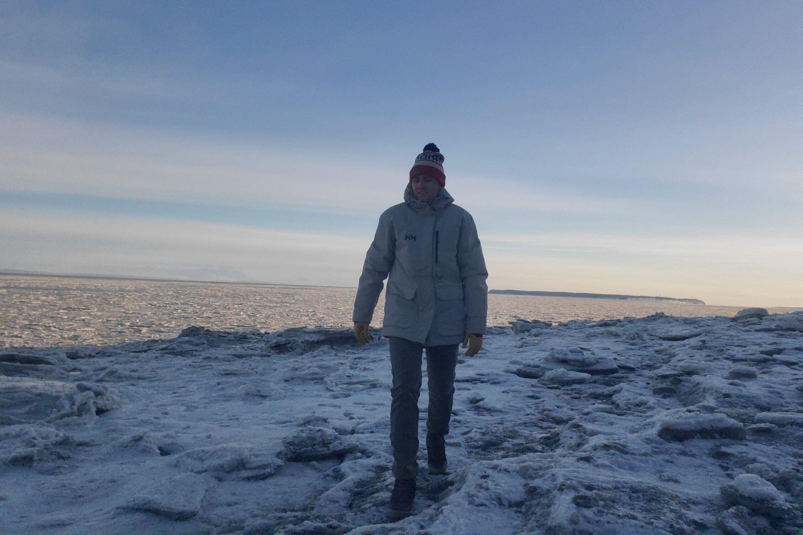 A man walks toward the camera on gray sea ice.