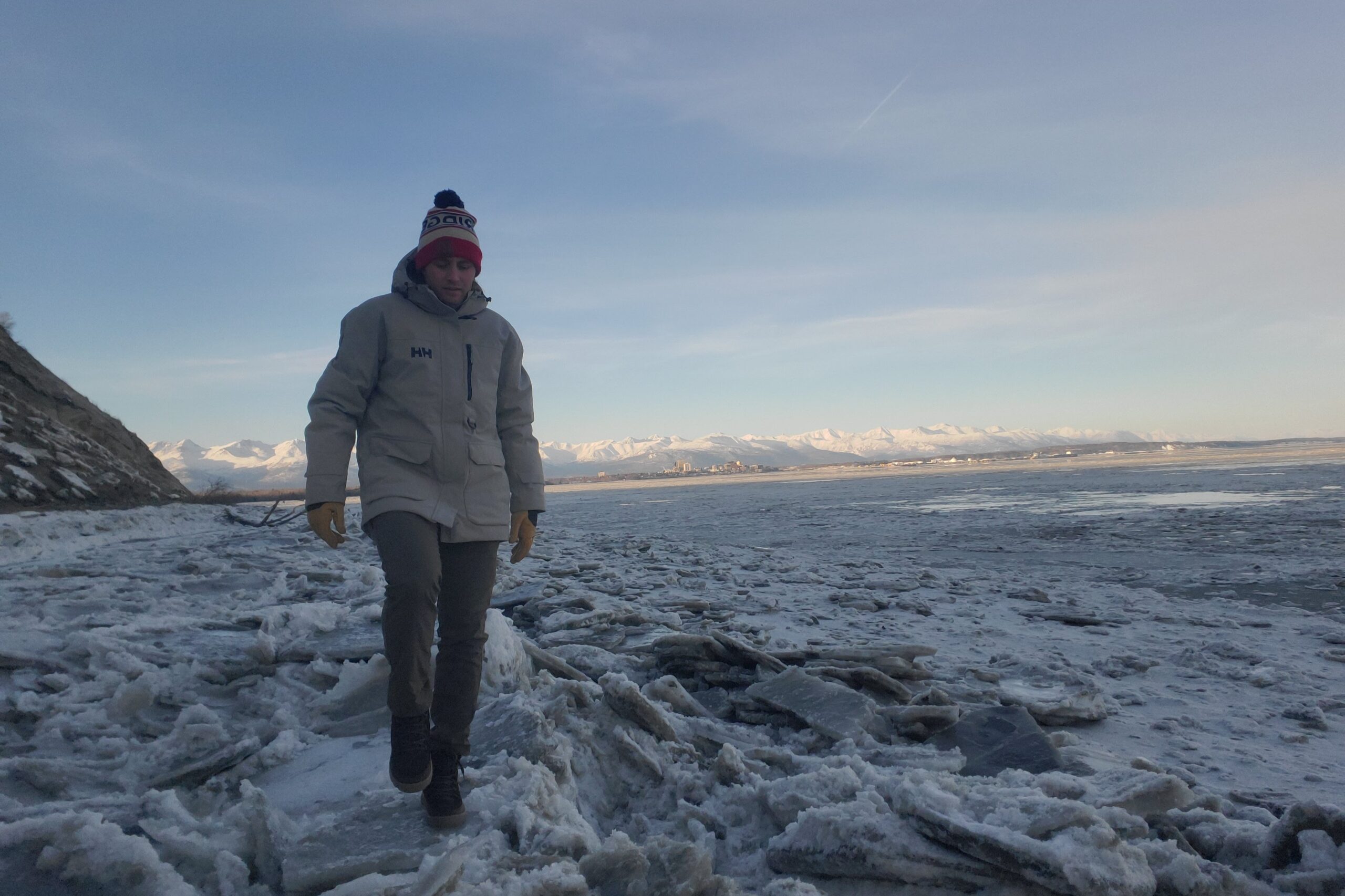 A man walks on plates of ice with mountains in the background.