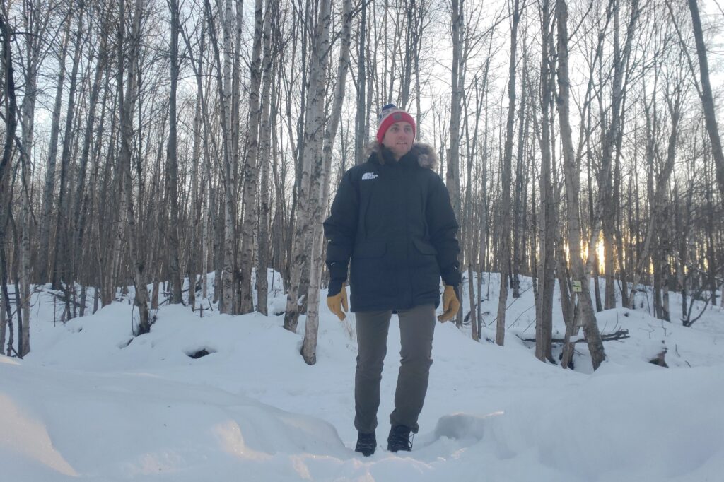 A man stands at sunset in a winter forest.