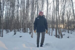 A man stands at sunset in a winter forest.