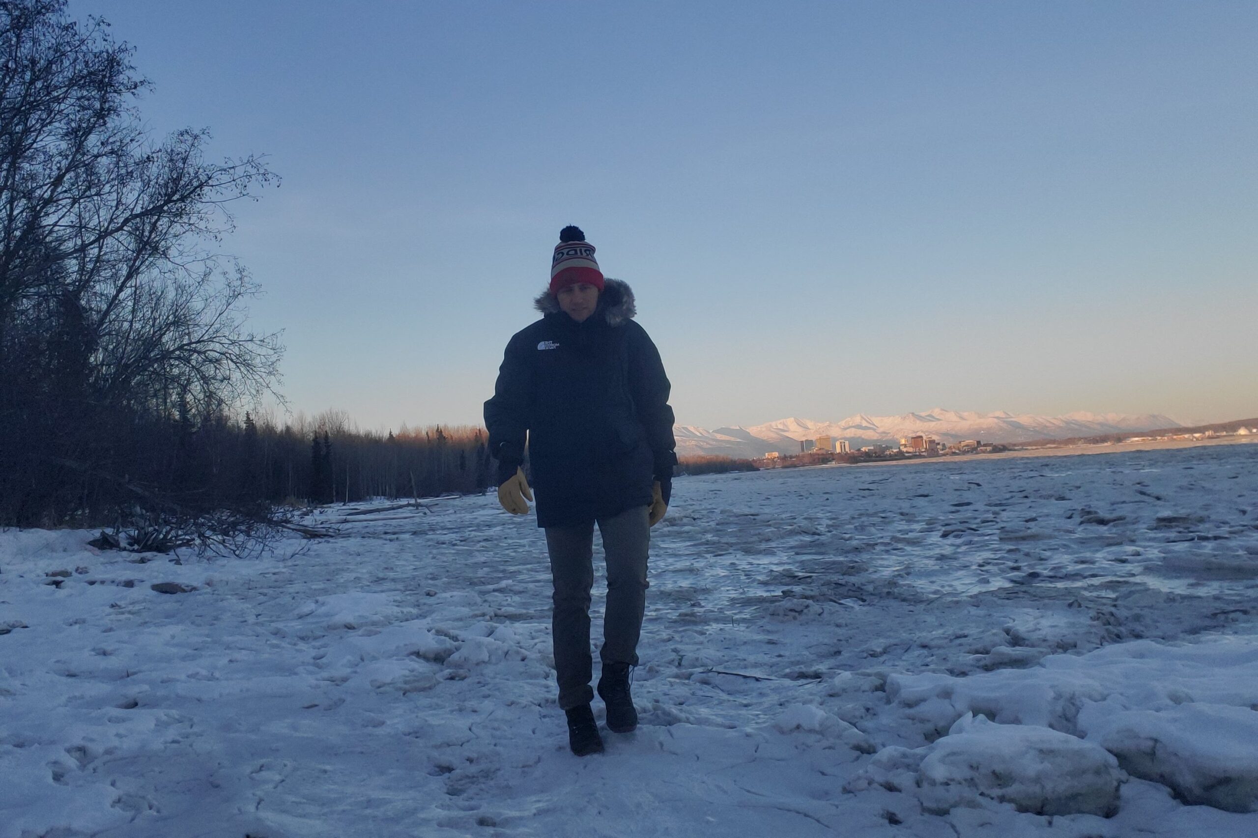 A man walks on ice with a city in the background.