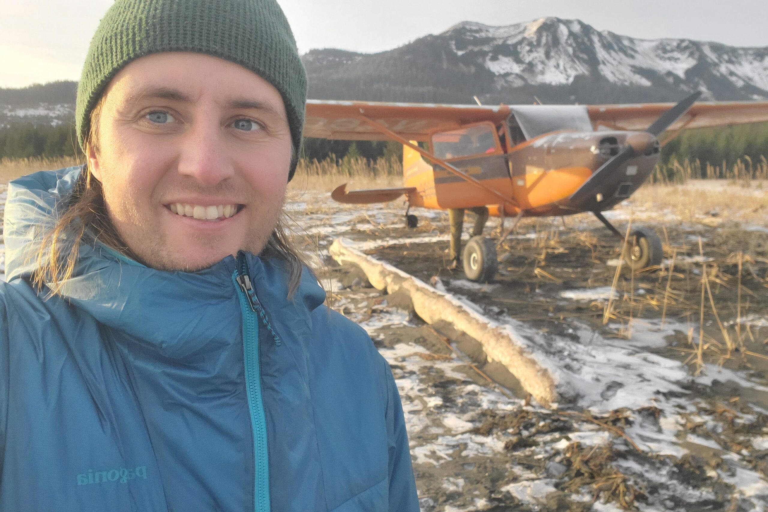 A man stands in front of a small plane parked on a beach