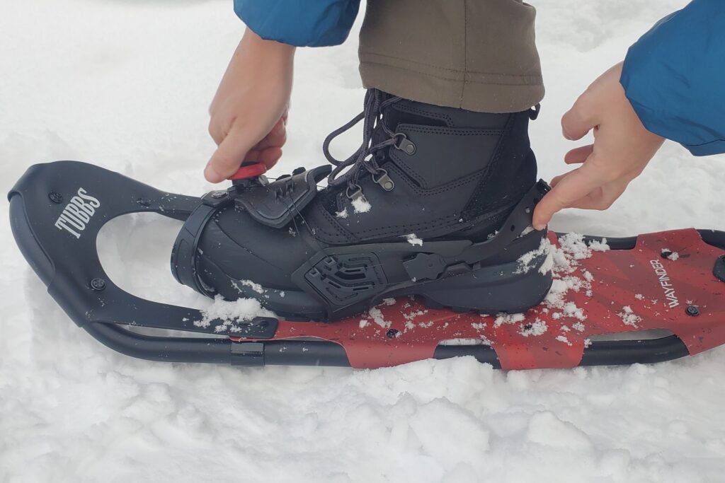 A man adjusts the binding on a pair of snowshoes.