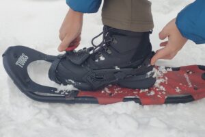 A man adjusts the binding on a pair of snowshoes.