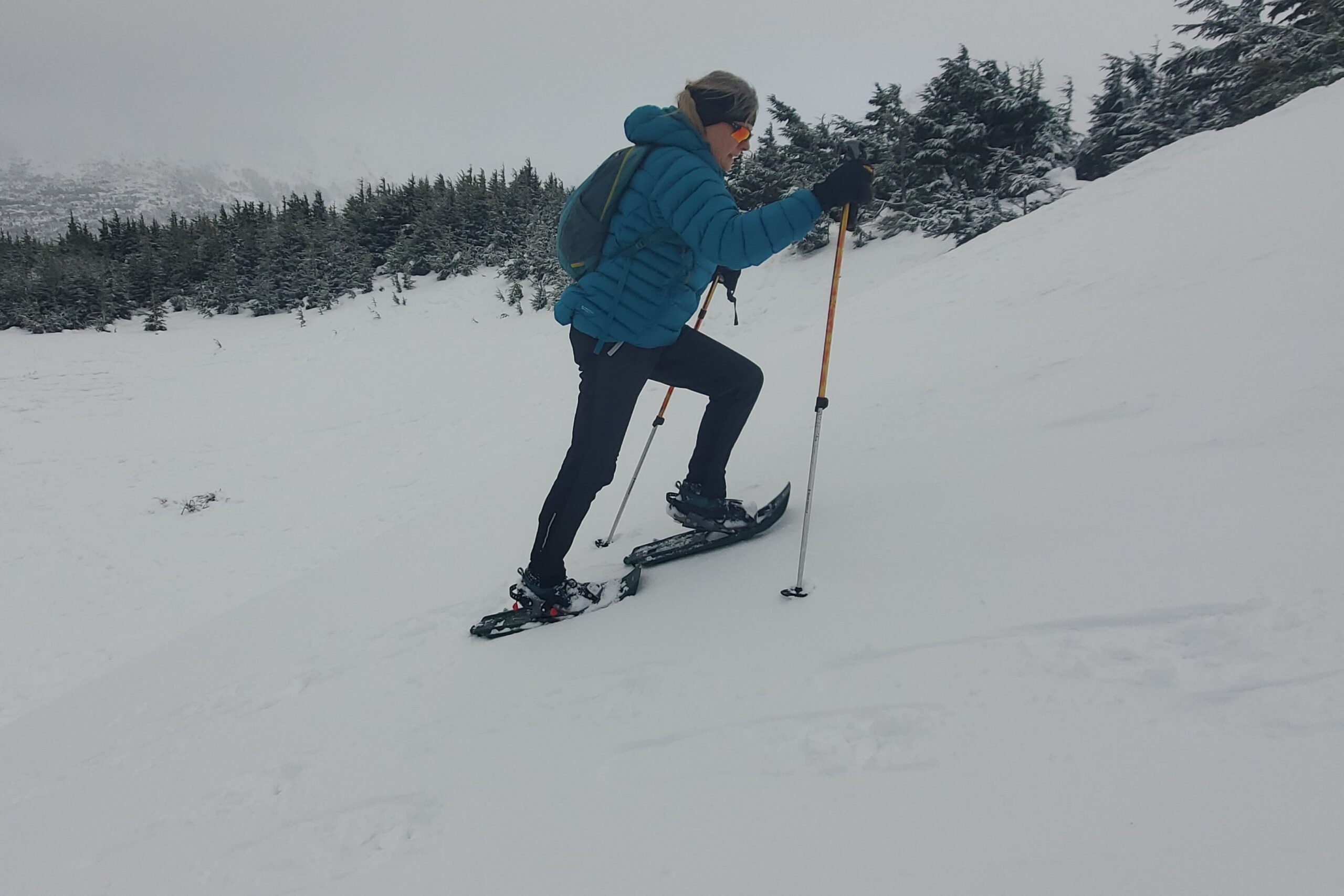 A woman hikes up a steep hill wearing snowshoes.