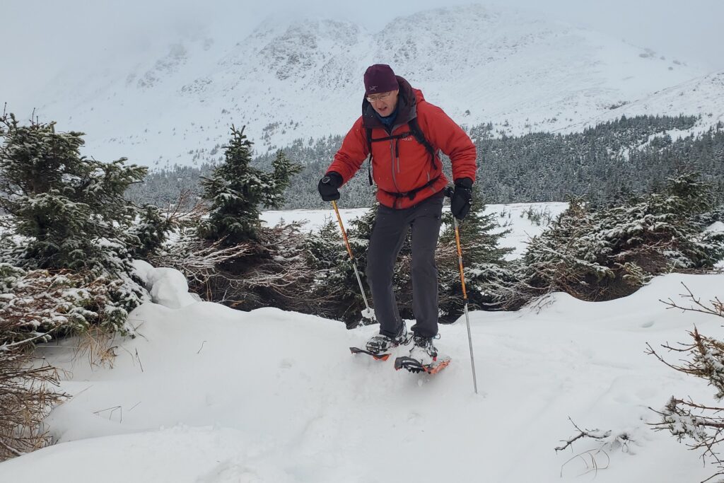 A man steps down a snow drift in snowshoes.