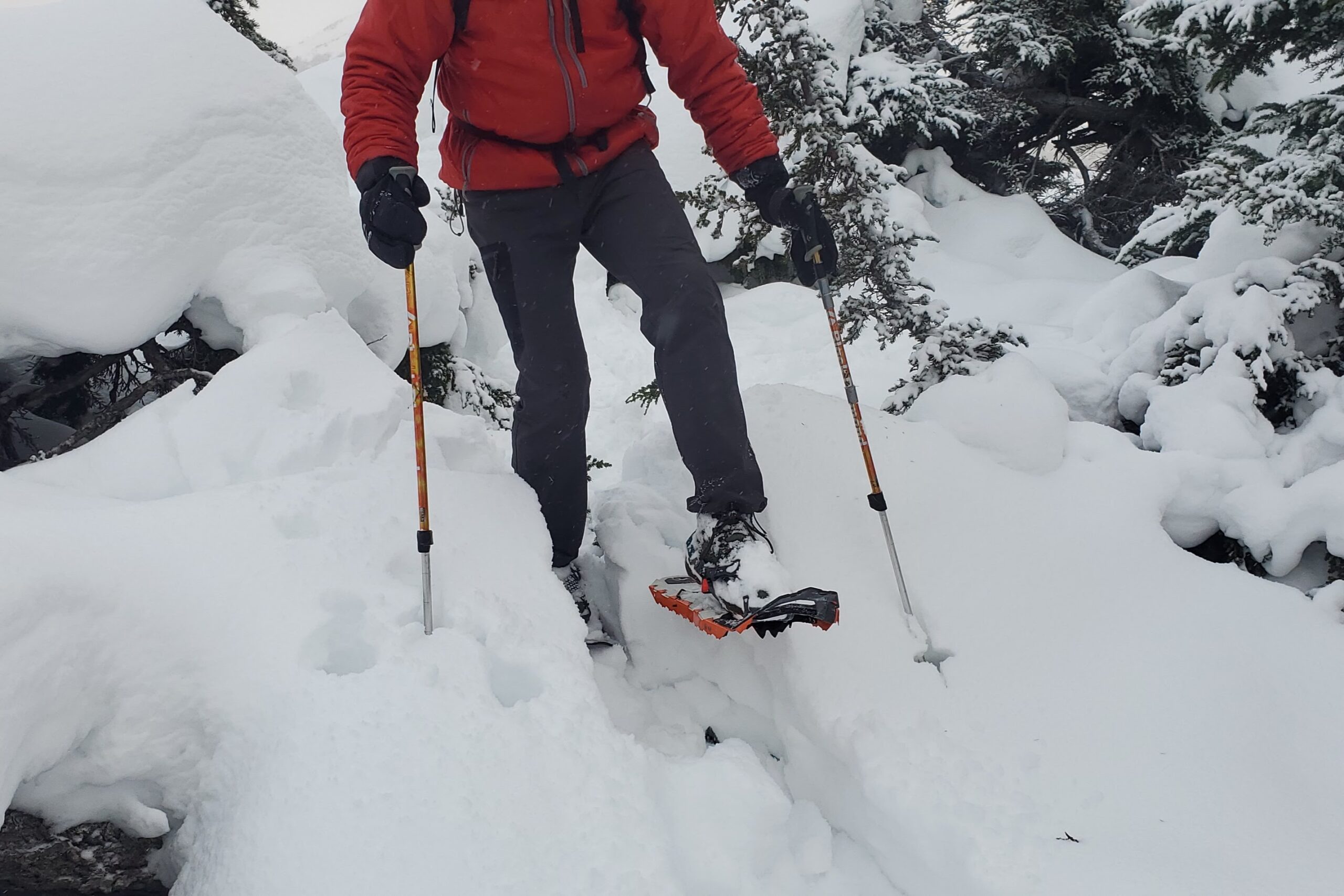 A man steps through a snow drift wearing snowshoes.