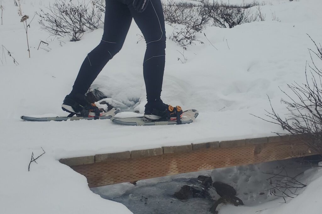 A person walks across a snow covered bridge while wearing snowshoes