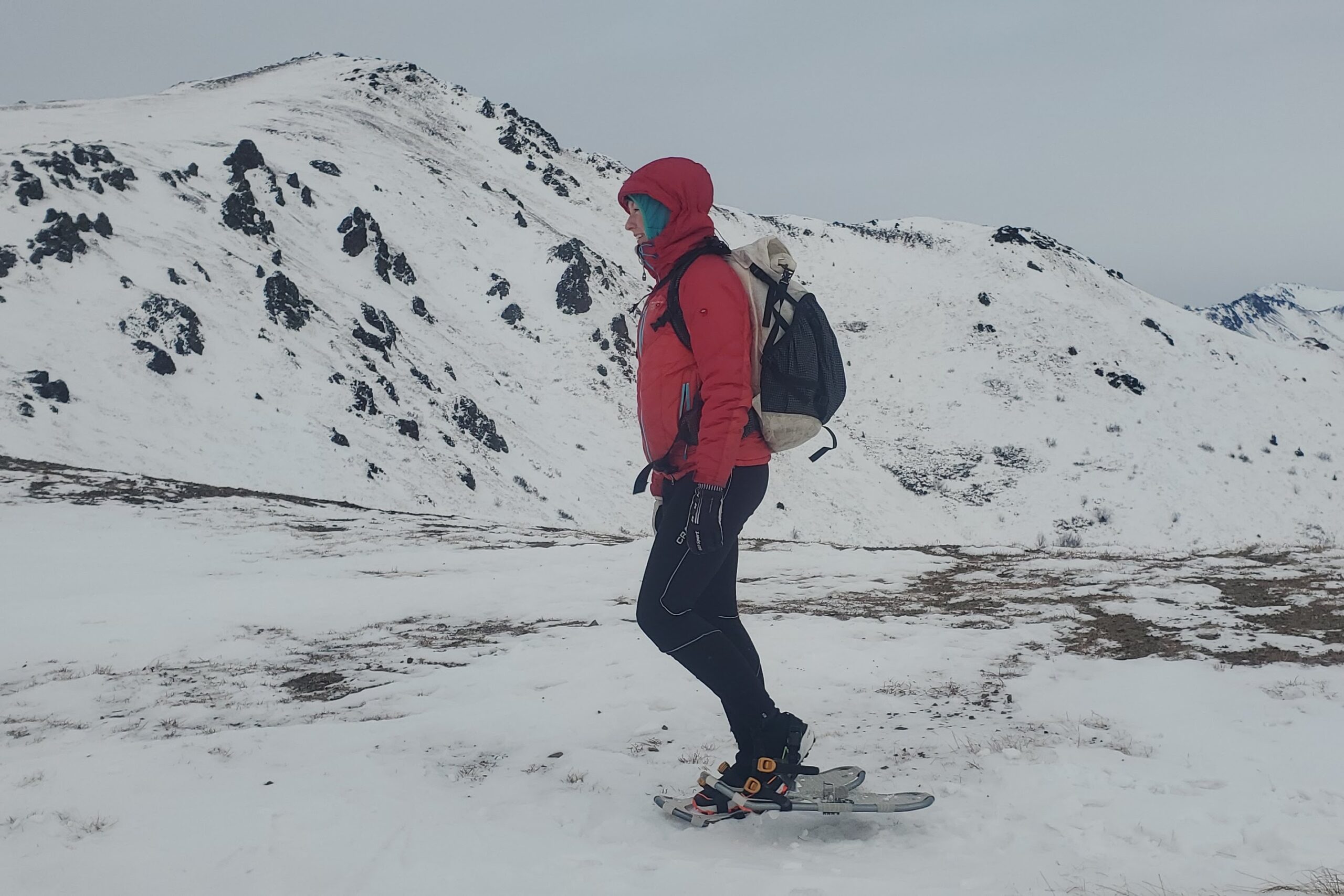 A woman walks on a ridgeline wearing snowshoes.