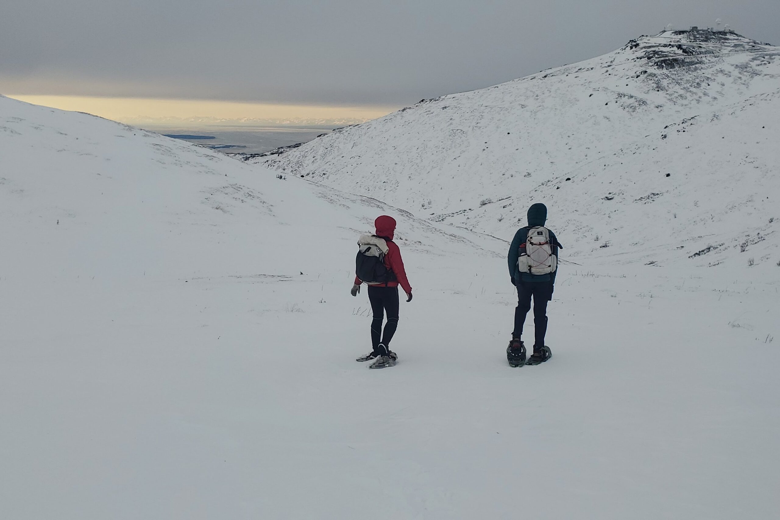 Two people walk down a mountainside in snowshoes.