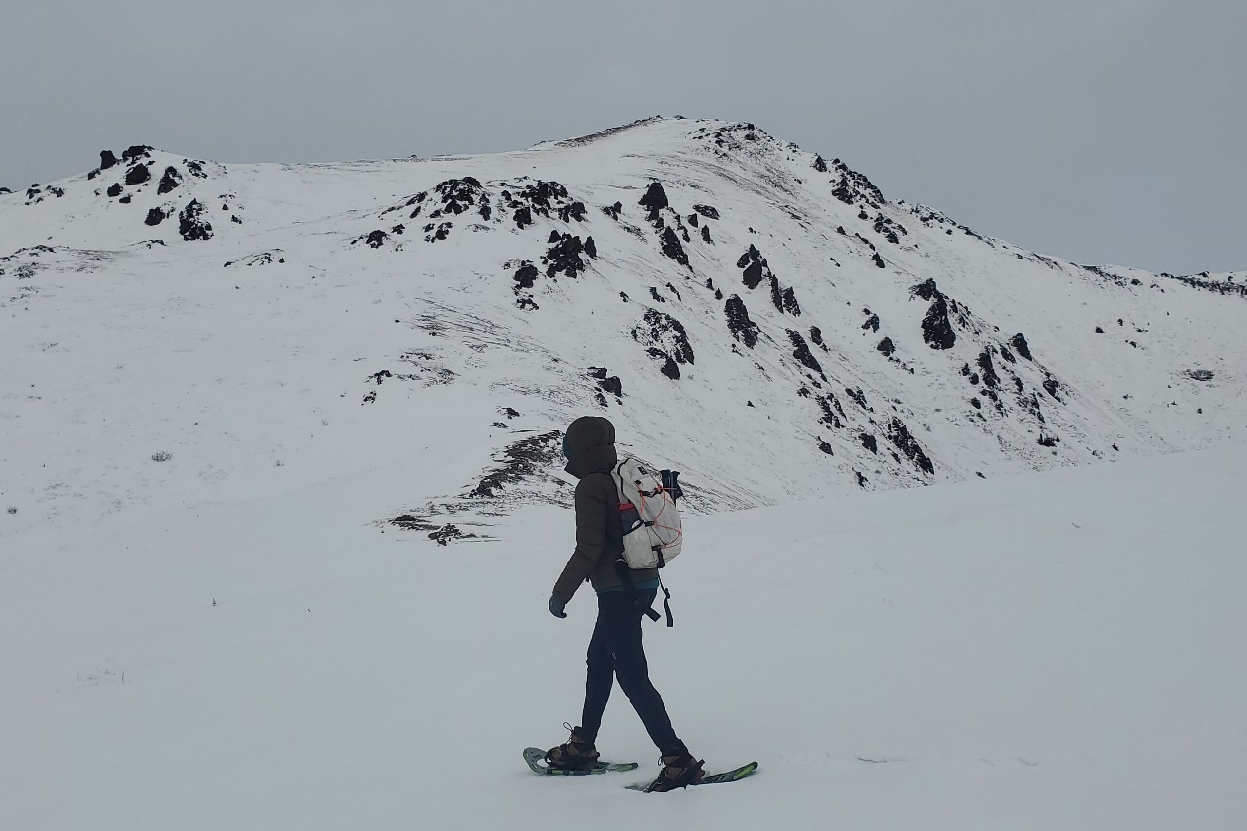 A woman walks past a mountain wearing snowshoes