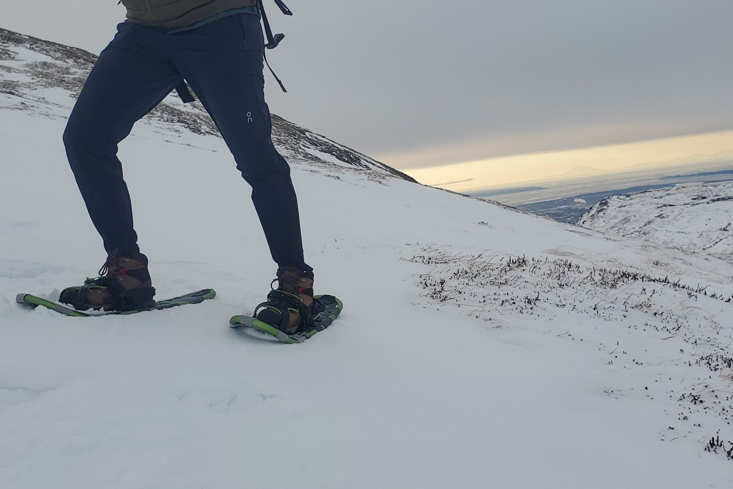 A person stands on a snowy hillside wearing snowshoes.