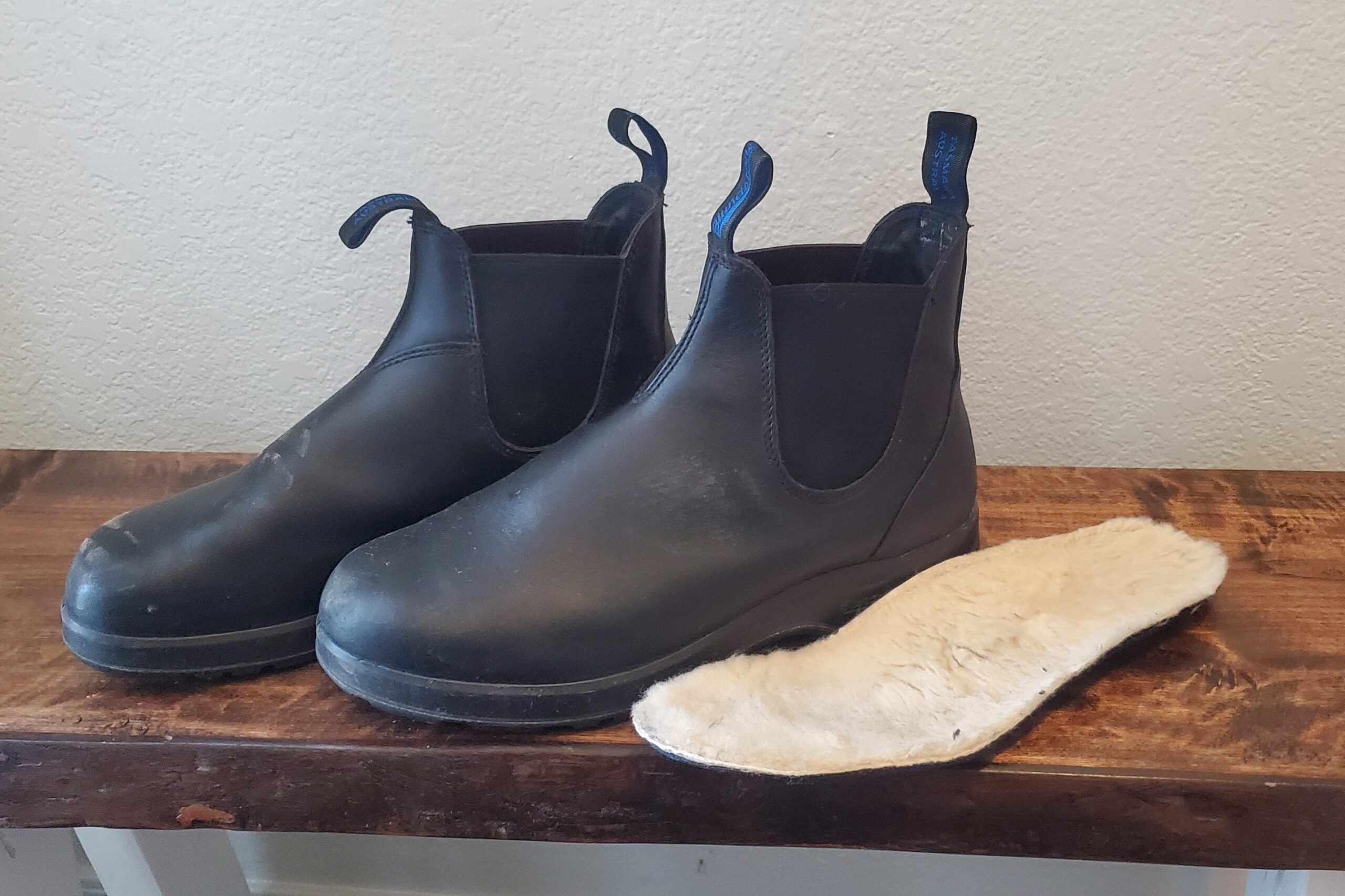 A pair of boots sitting on a bench with the insole next to them.