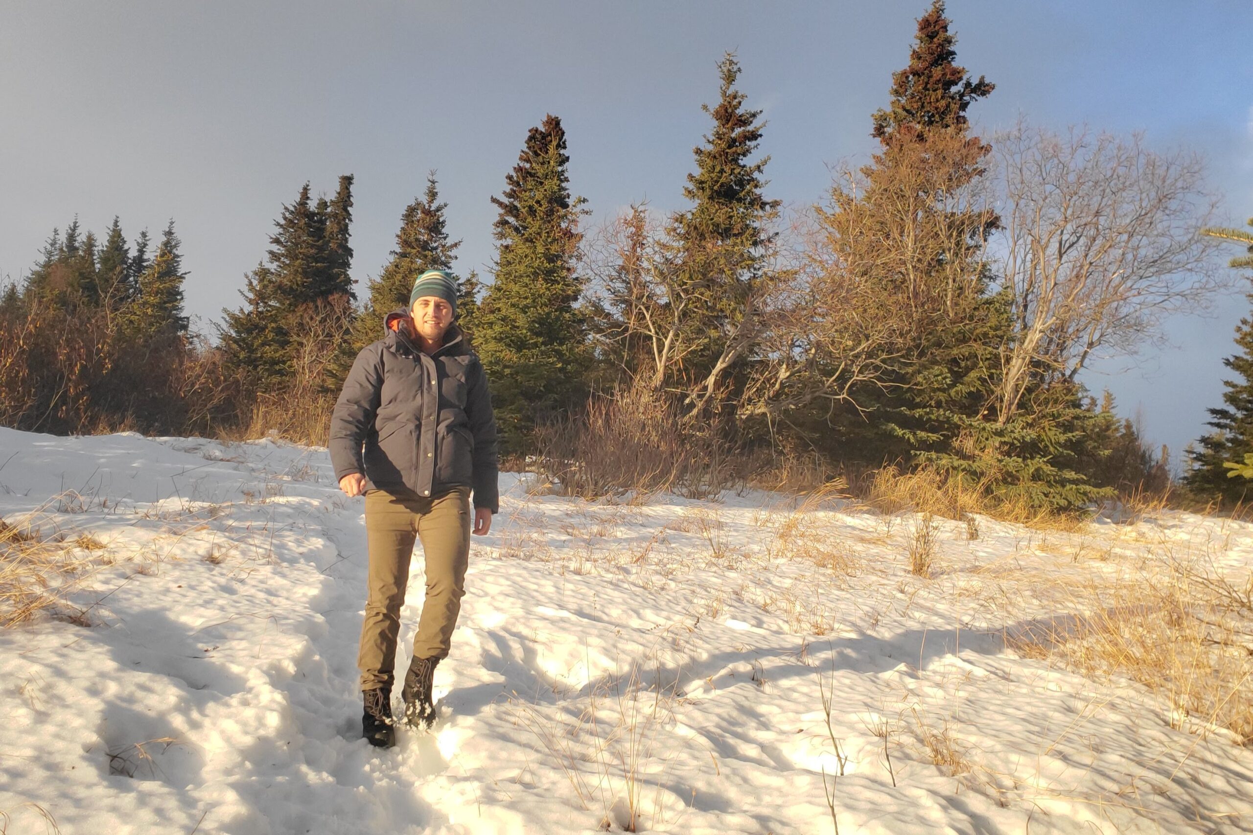 A man walks down a snowy trail in sunlight.