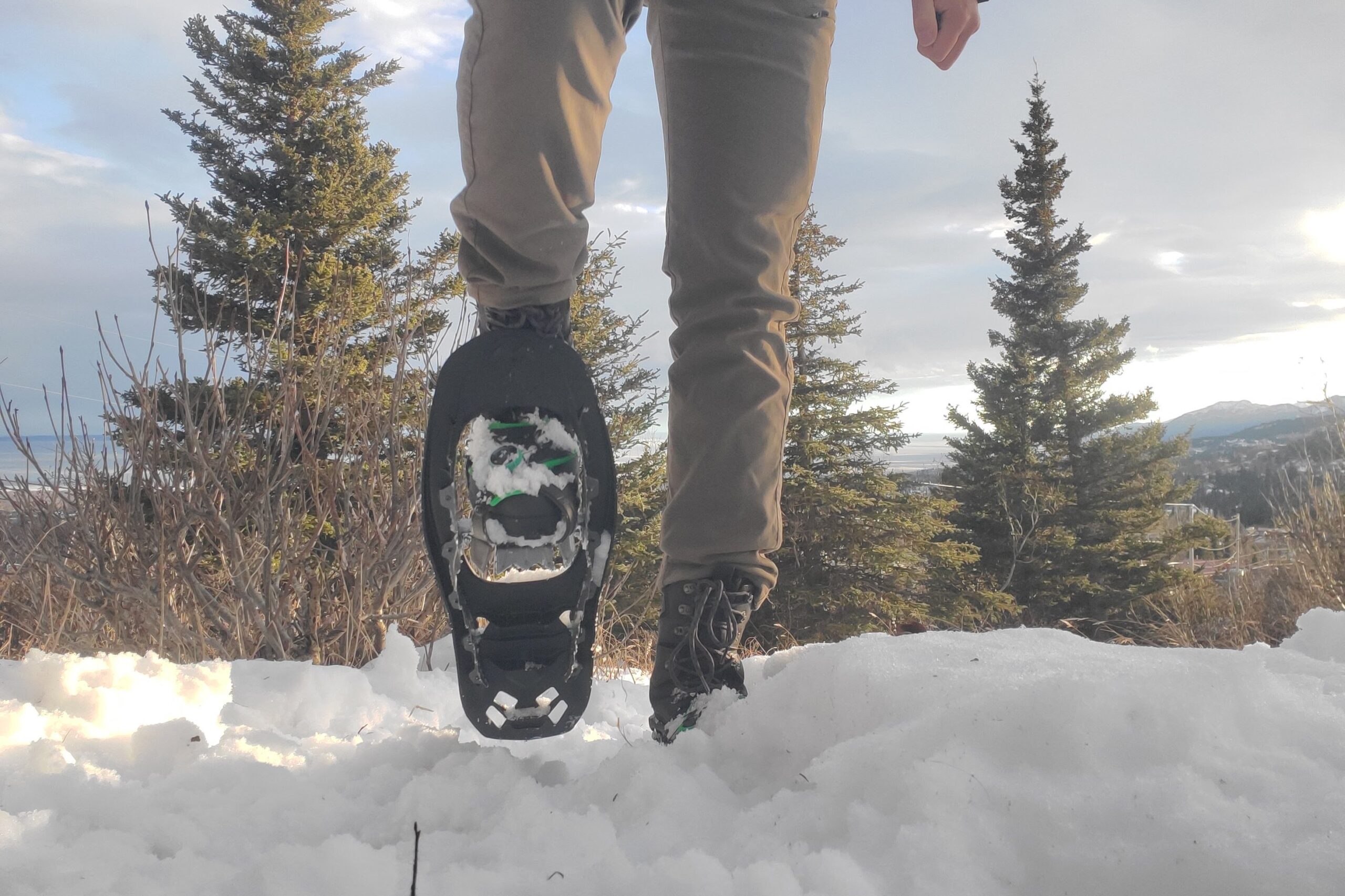 A man walks uphill on snow while wearing snowshoes.