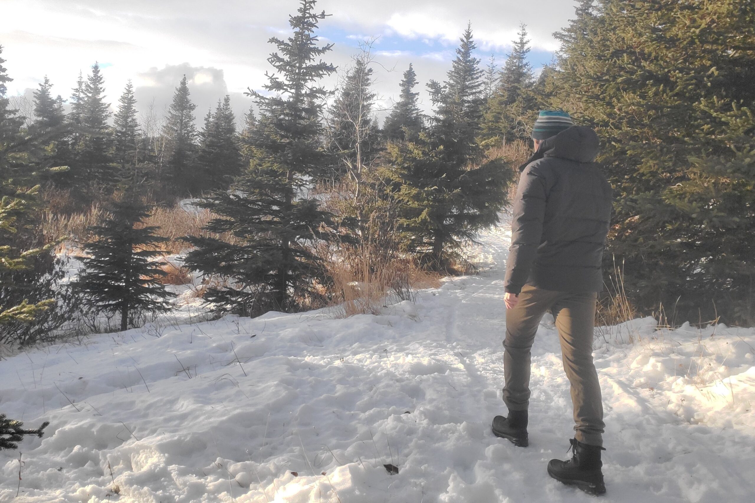 A man walks away from the camera on a snow covered trail.