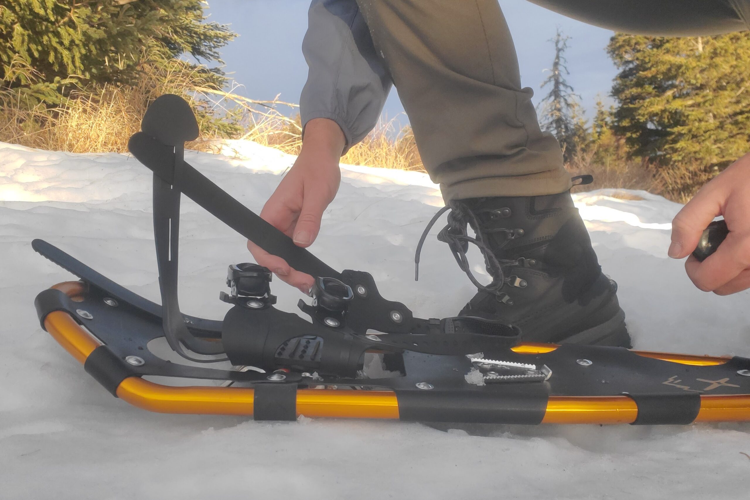 A man puts on a pair of snowshoes with ratchet bindings.