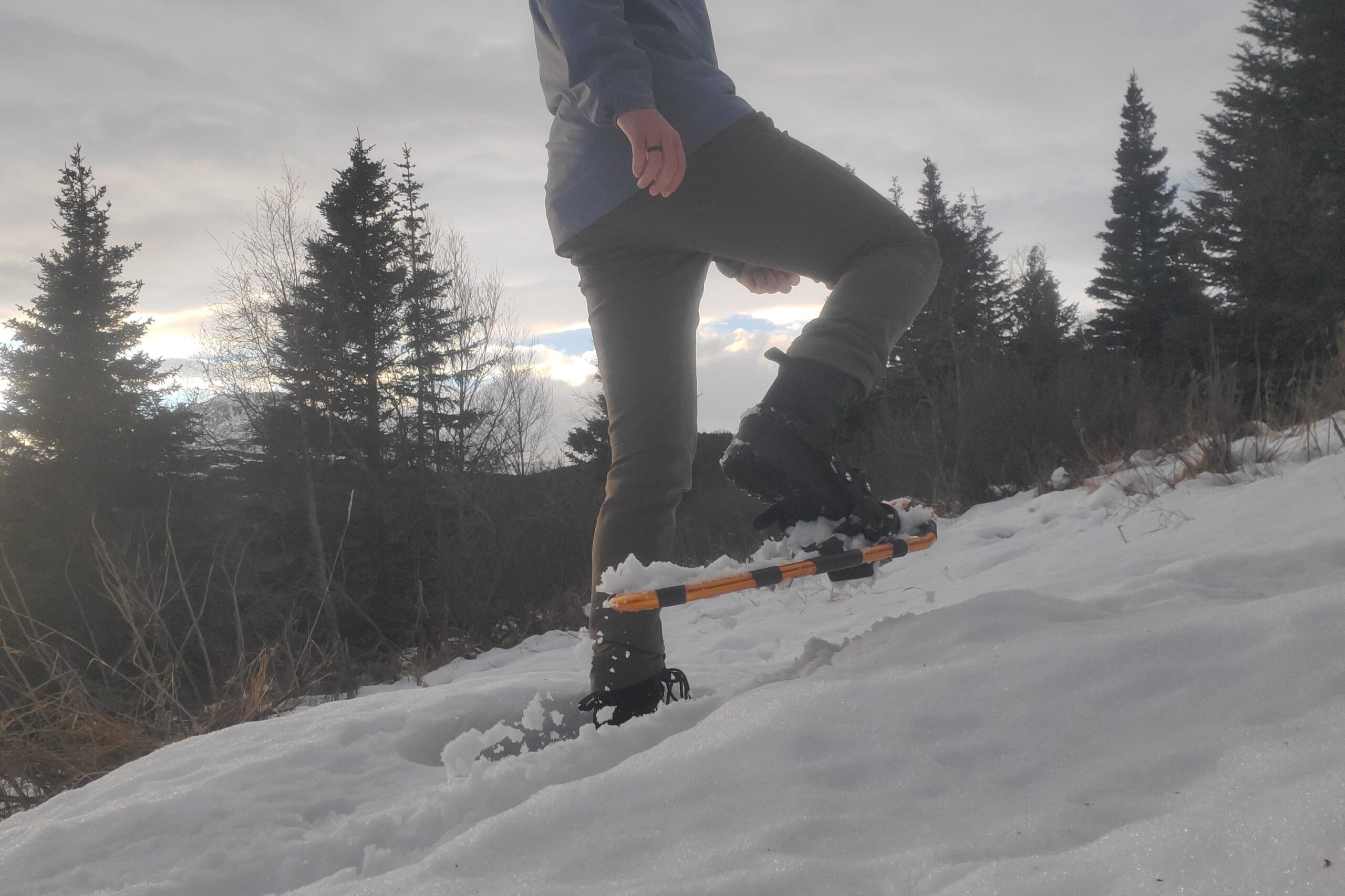 A man steps through deep snow while wearing snowshoes.