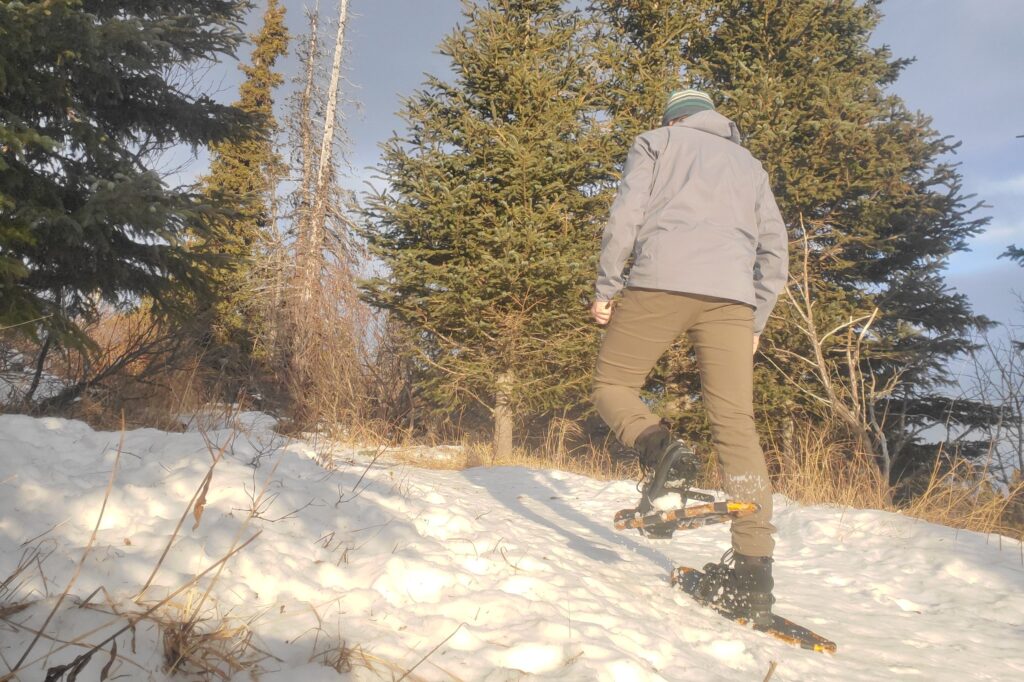 A man walks uphill while wearing snowshoes.