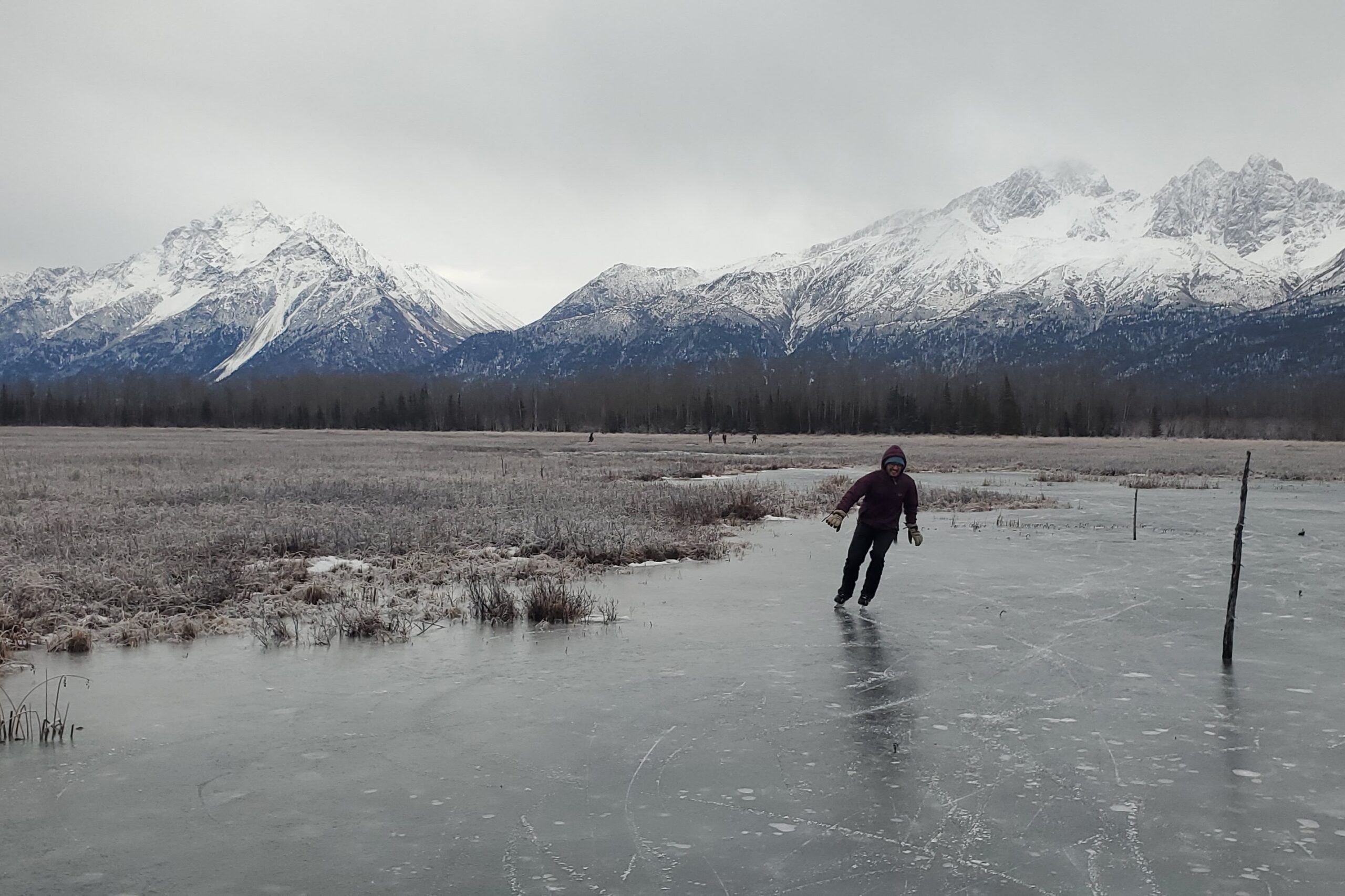 A man ice skates with mountains in the background.