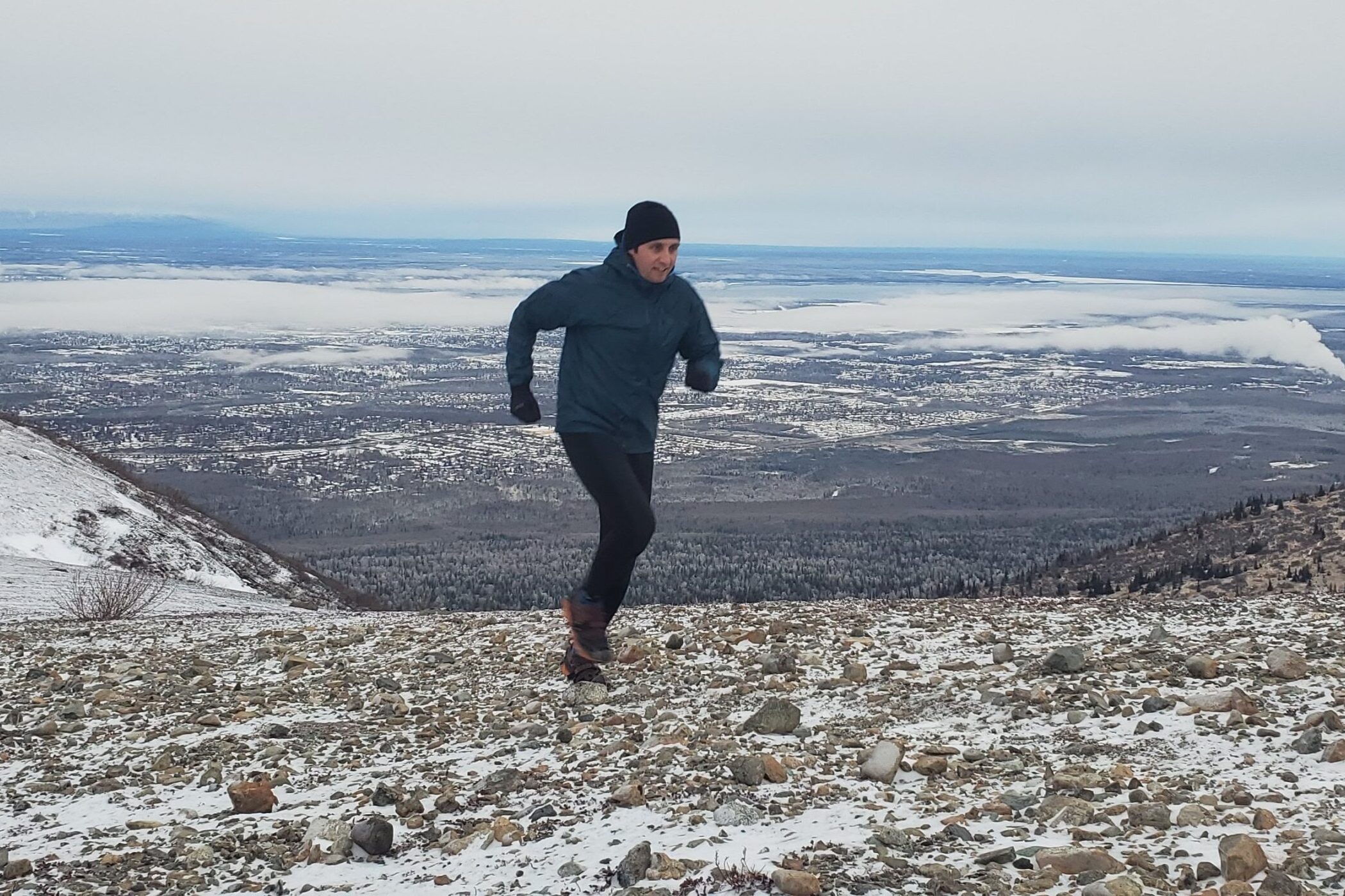 A man runs up a mountain trail with the ocean behind him.