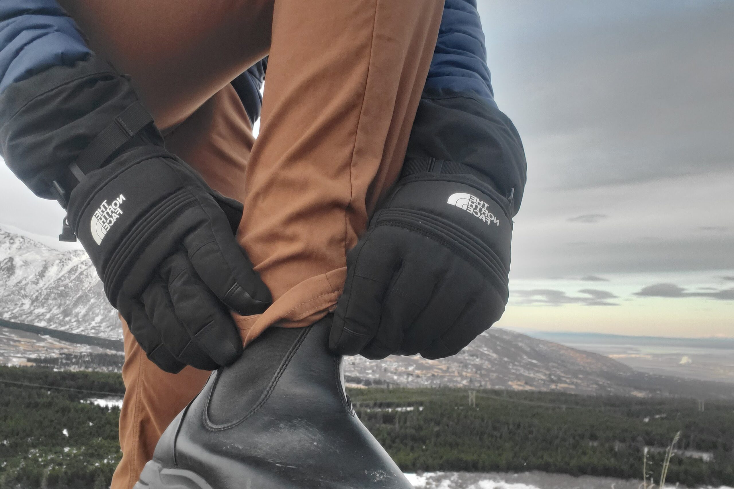 A man wearing gloves adjust his boot.