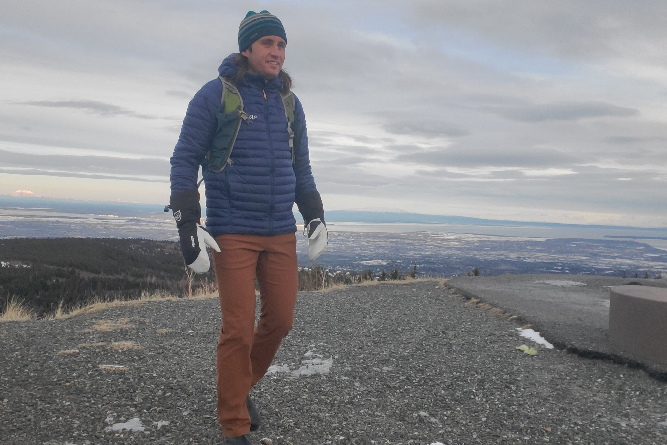 A man walks on a trail with a city below in the background.