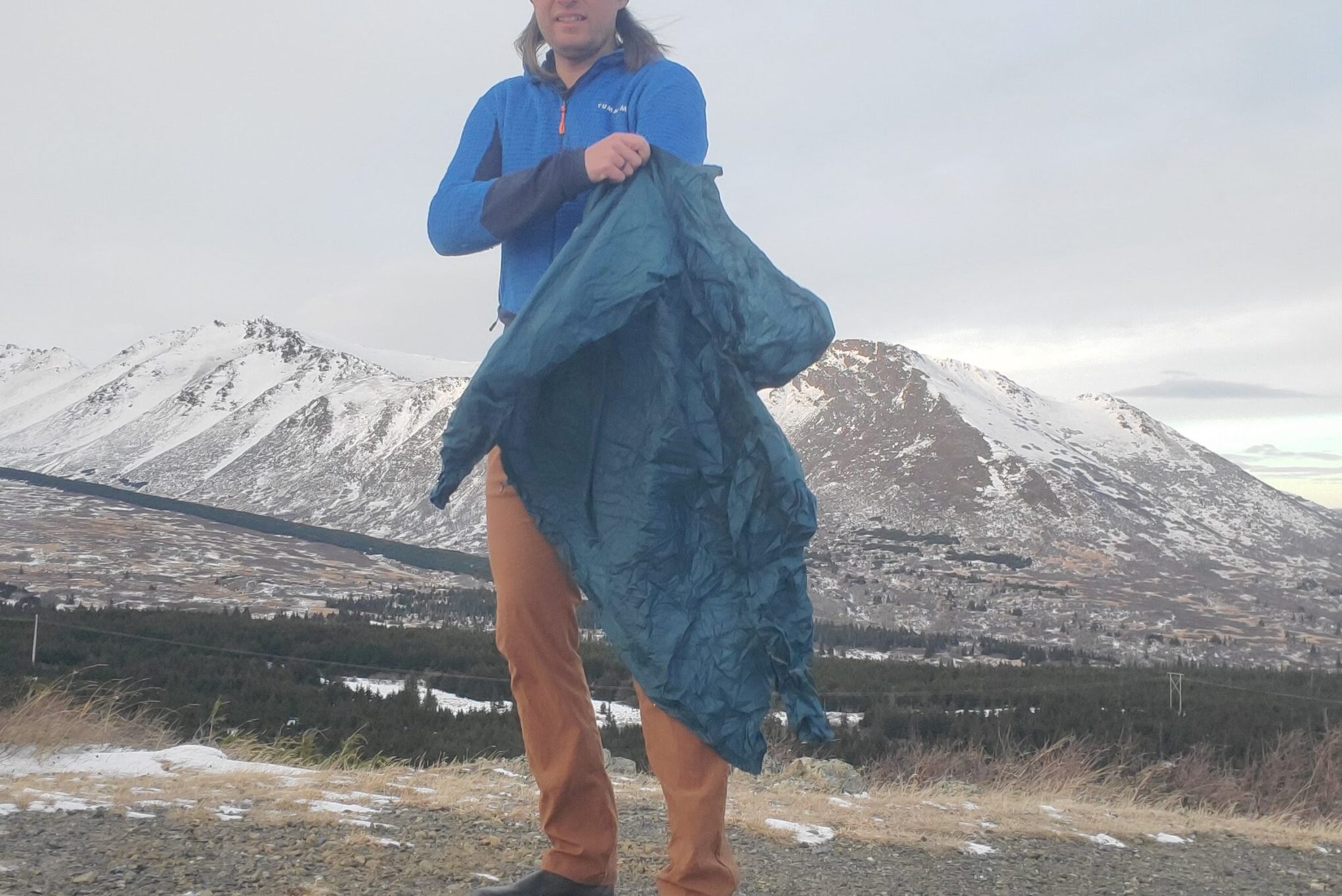 A man puts on his rain jacket in front of a mountain landscape.