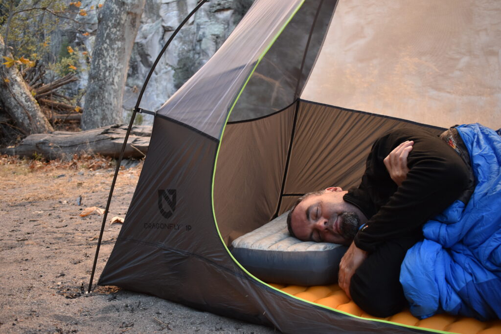 The Aeros Down Deluxe pillow supports the author's head and neck as he sleeps on his side in a tent pitched in front of gray cliffs