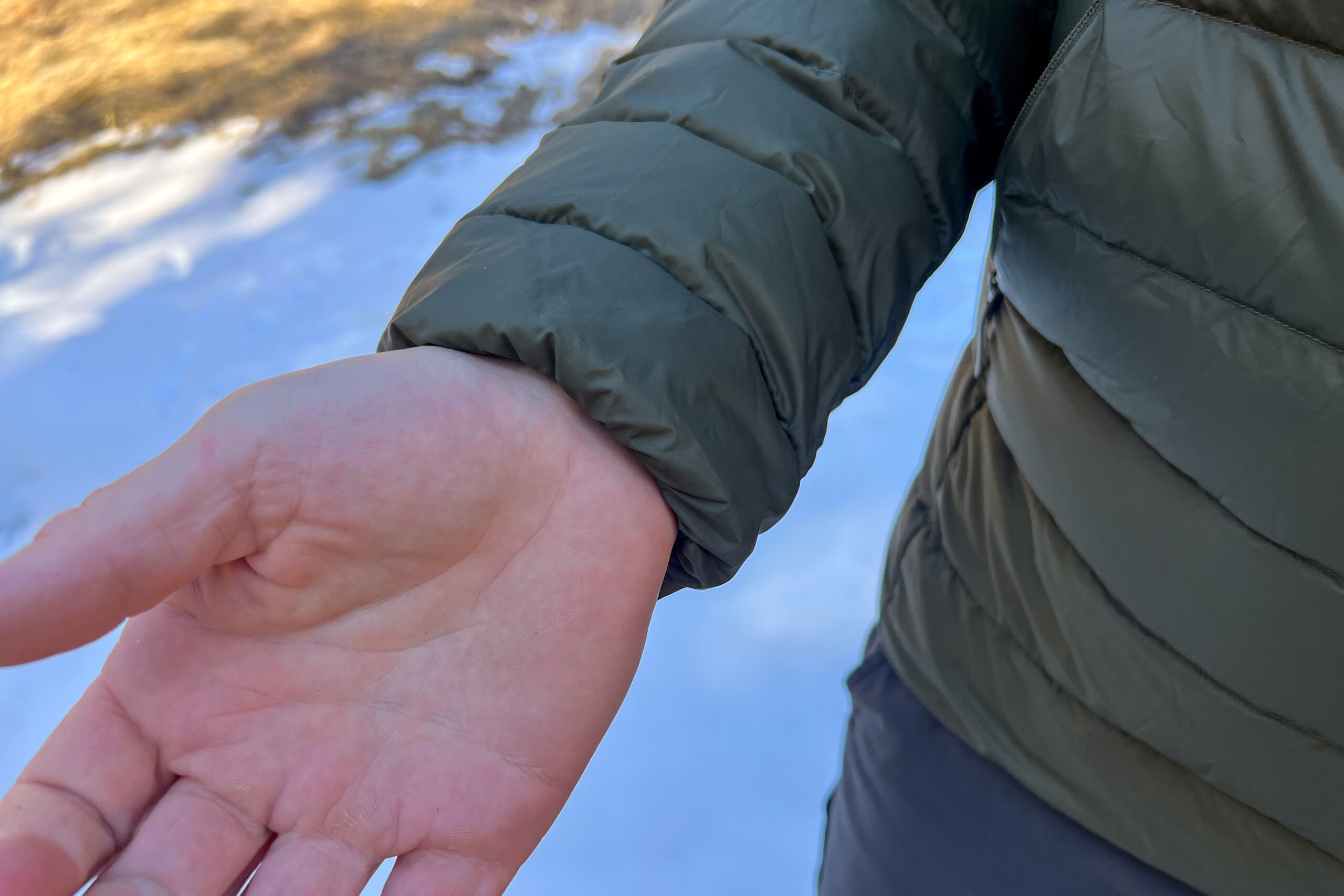 Close-up of the Arc'teryx Cerium Hoody’s elastic cuff snugly fitting around a person’s wrist, with a snowy background visible.