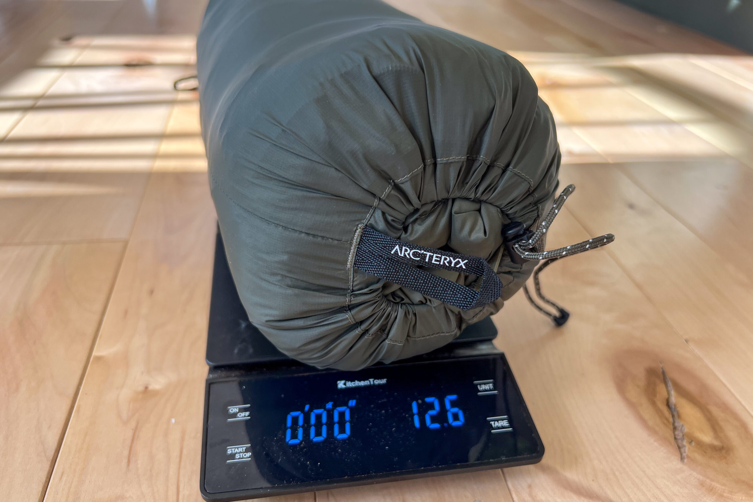 The Arc'teryx Cerium Hoody packed into its stuff sack, sitting on a digital scale displaying a weight of 12.6 ounces.