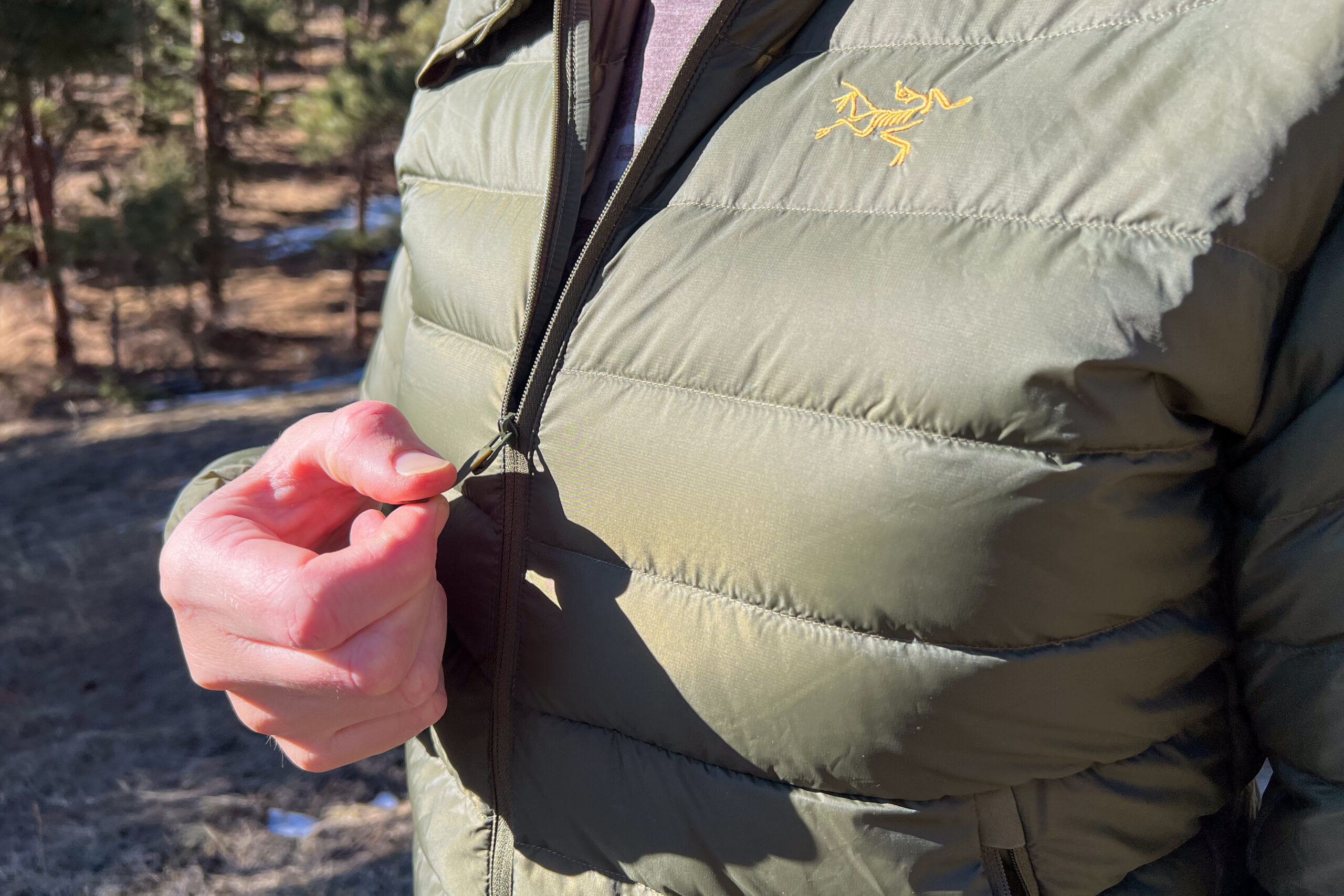 Close-up of a person pulling the lightweight zipper on the Arc'teryx Cerium Hoody, highlighting its small and minimal design.