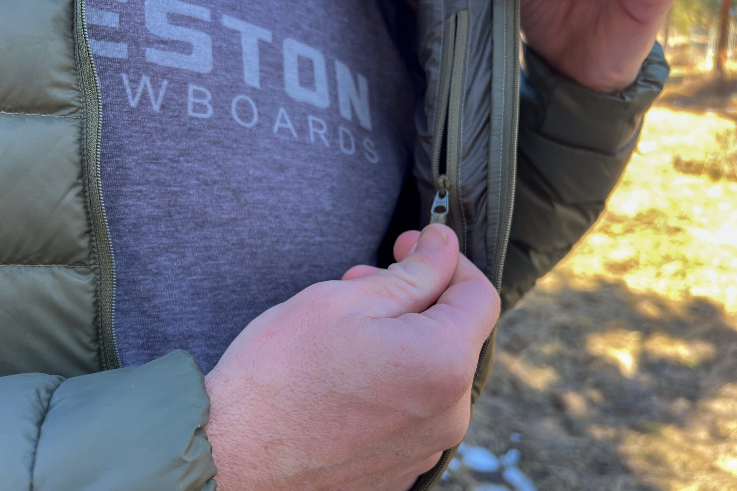 Close-up of a person holding the lightweight zipper of the Arc'teryx Cerium Hoody, showing the small zipper design and fine stitching details on the jacket.