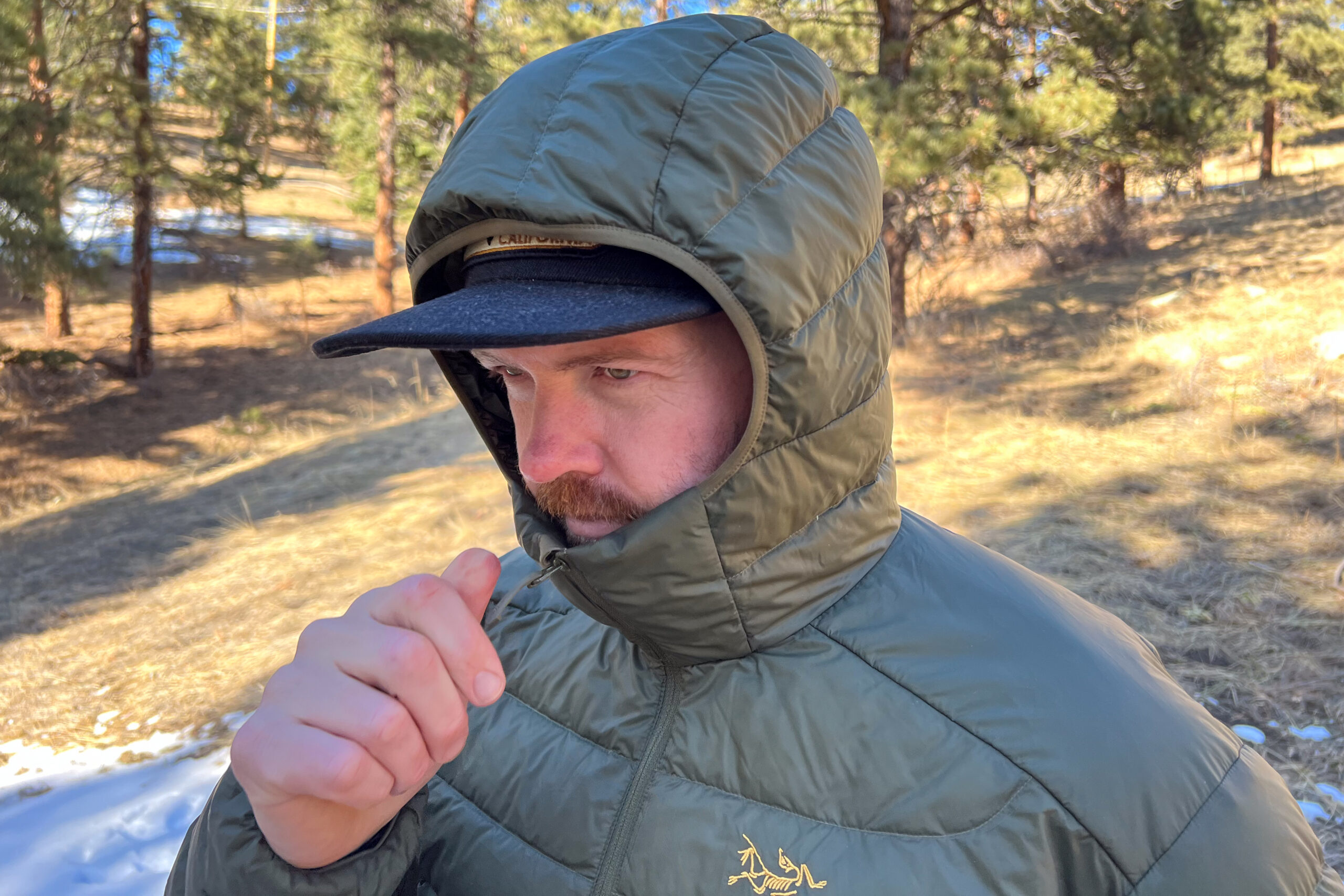 Person wearing the Arc'teryx Cerium Hoody with the hood up, showing its snug fit and adjustable design in an outdoor setting.