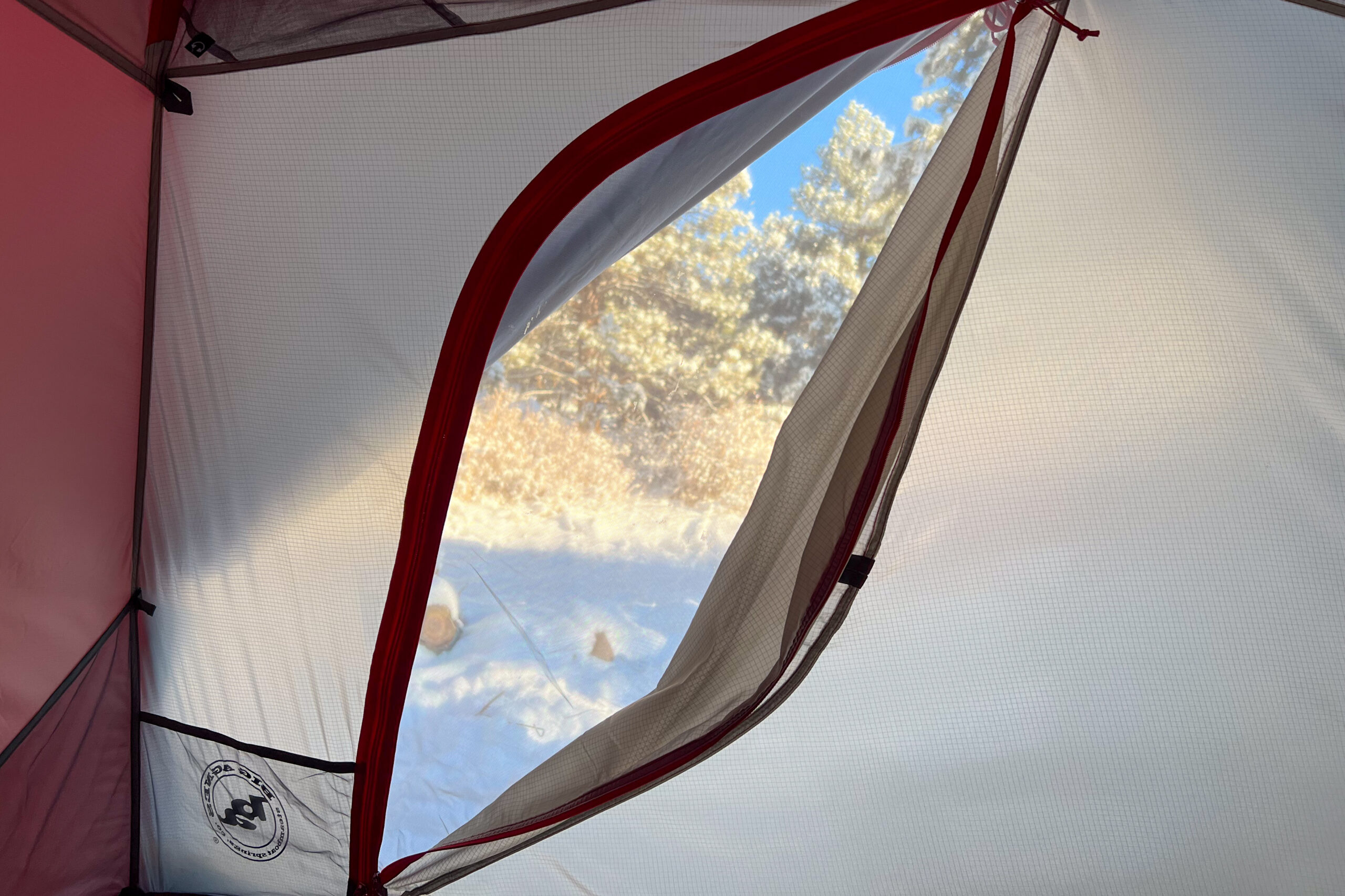 Interior view from inside the Big Agnes Copper Spur Expedition tent, looking through a mesh window at snowy trees.